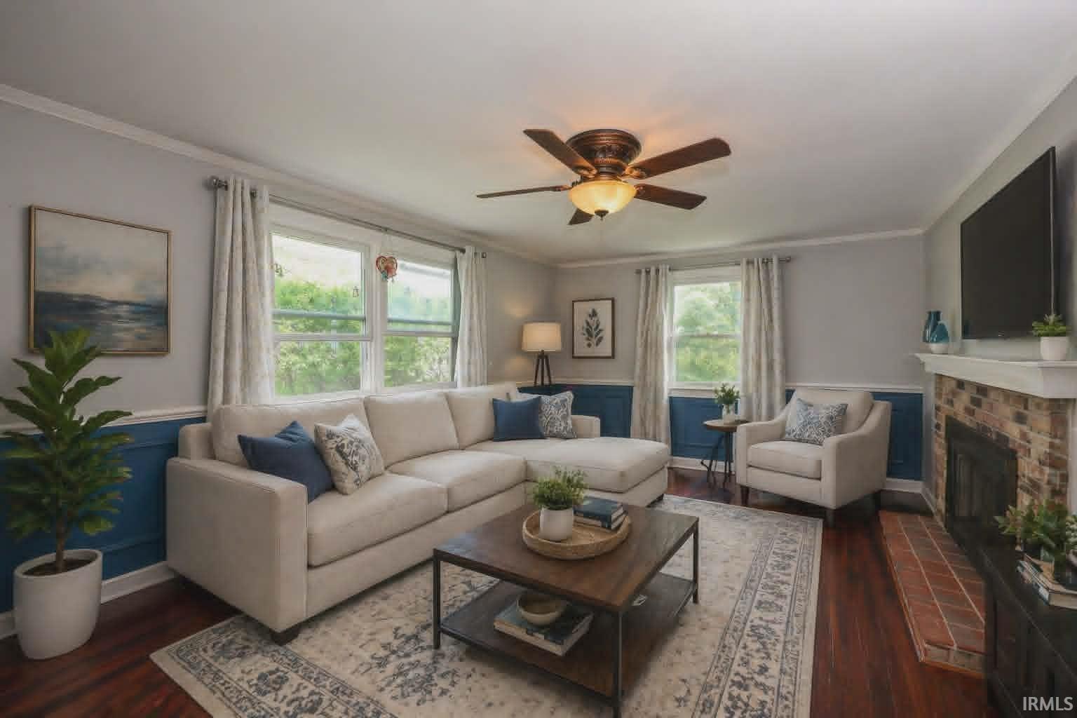 Inviting living area featuring rich wood-finish flooring, a brick fireplace with a white mantle, and dual windows