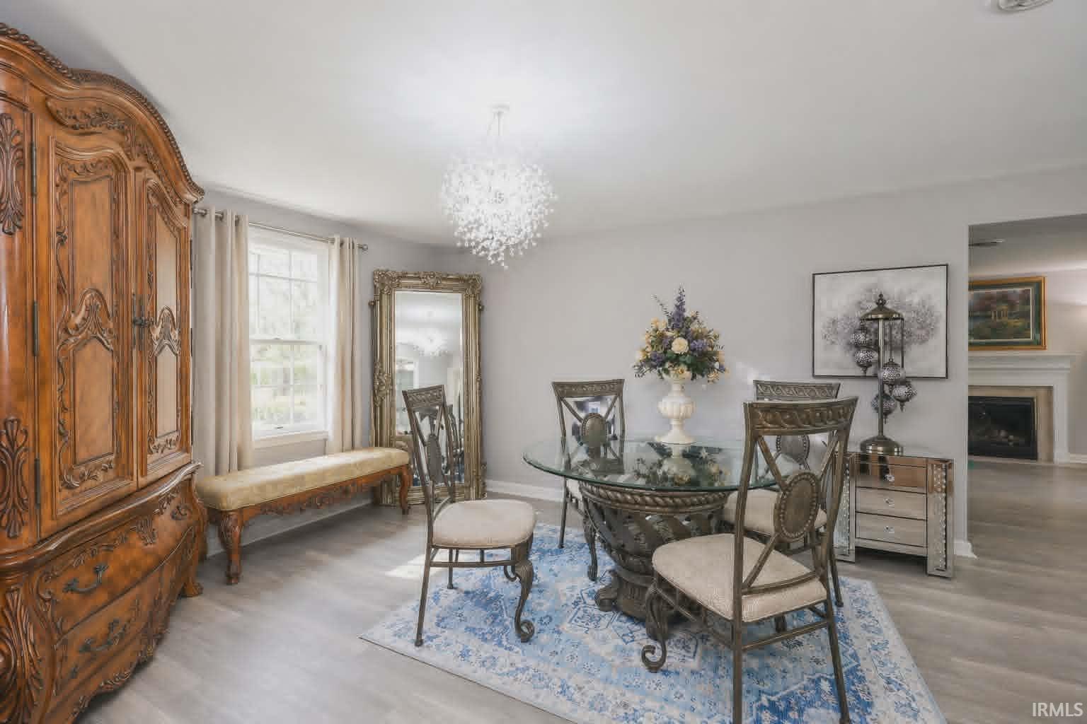 Dining area featuring light wood-finish flooring, a contemporary chandelier, two windows with drapes, and an opening to a room with a fireplace