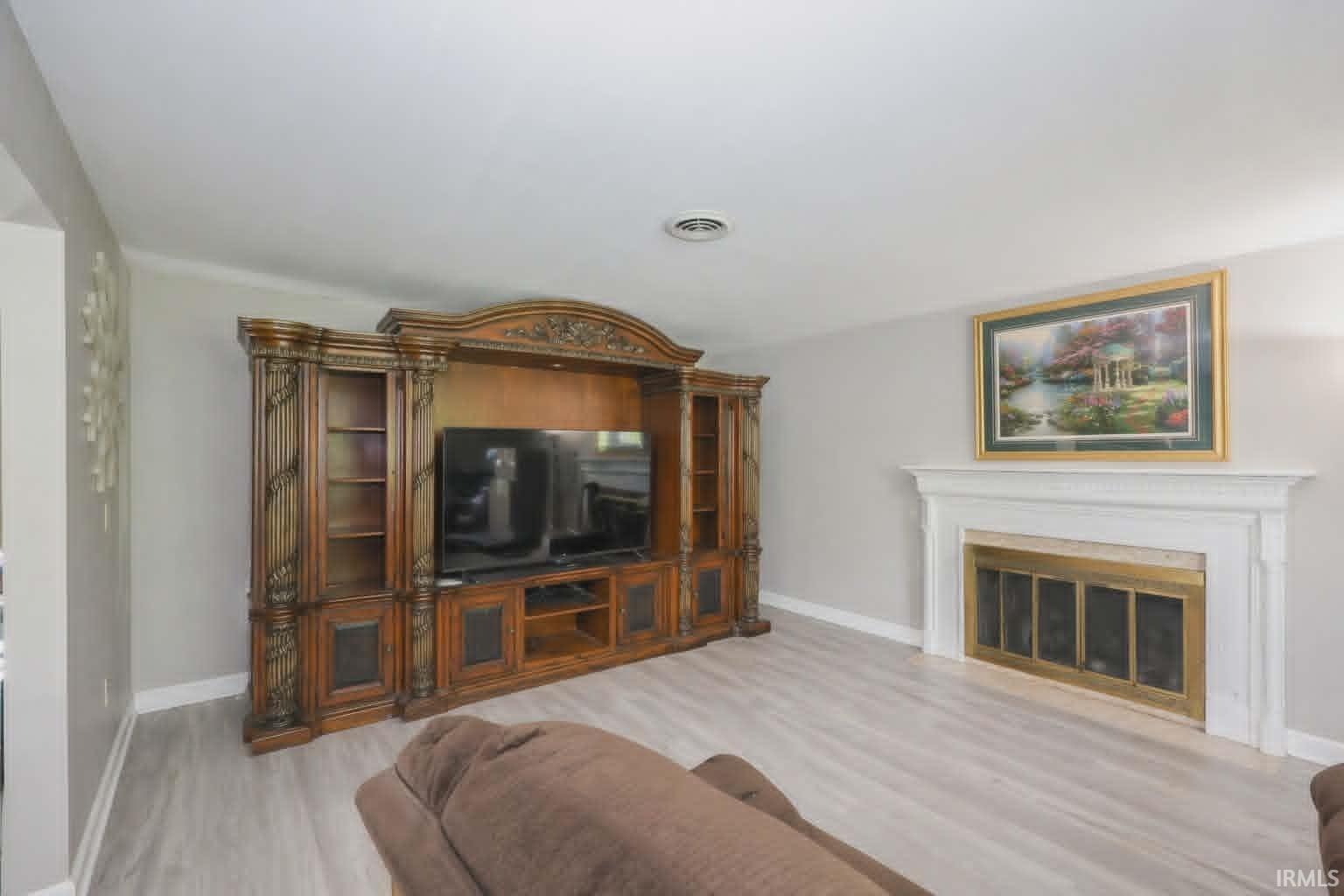 Living area featuring wood-finish flooring, a white mantel, and a fireplace with a brass-toned screen