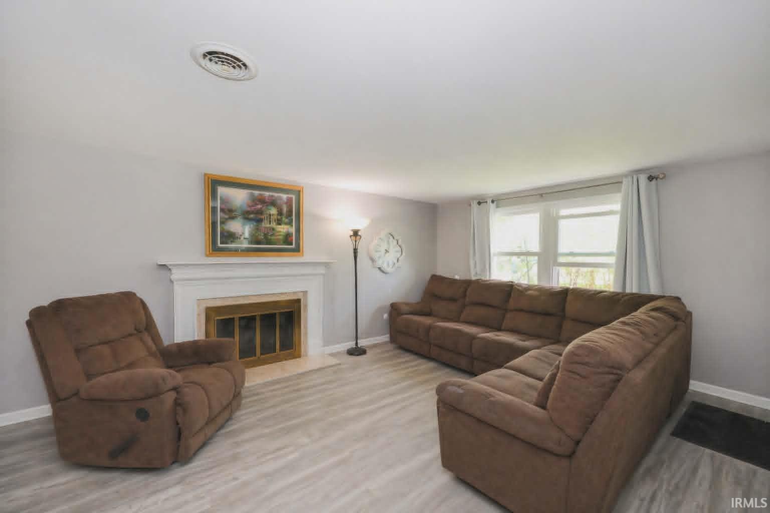 Living area featuring a fireplace with a white mantel, light gray walls, wood-finish flooring, and white window trim
