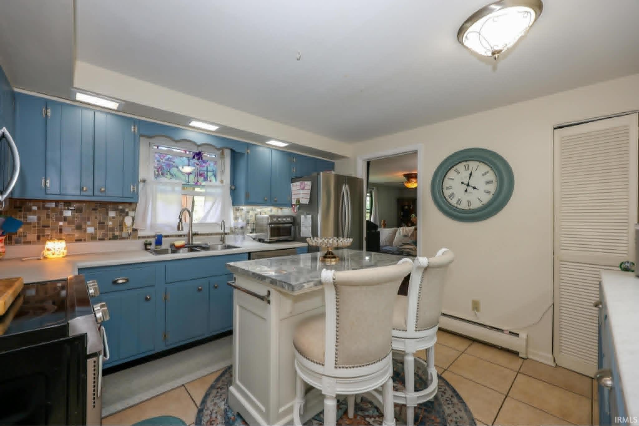 Kitchen featuring a central island with a stone countertop, blue cabinetry, a mosaic tile backsplash, stainless steel appliances, and tile flooring