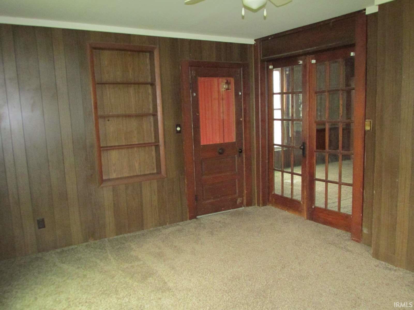 Carpeted interior space featuring wood-finish paneling, a built-in shelving unit, and a ceiling fan