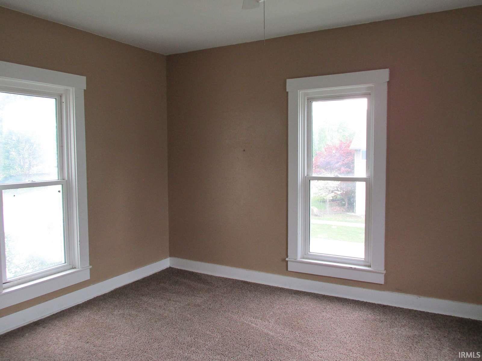 Room featuring two windows with white trim, tan painted walls, and brown carpet flooring