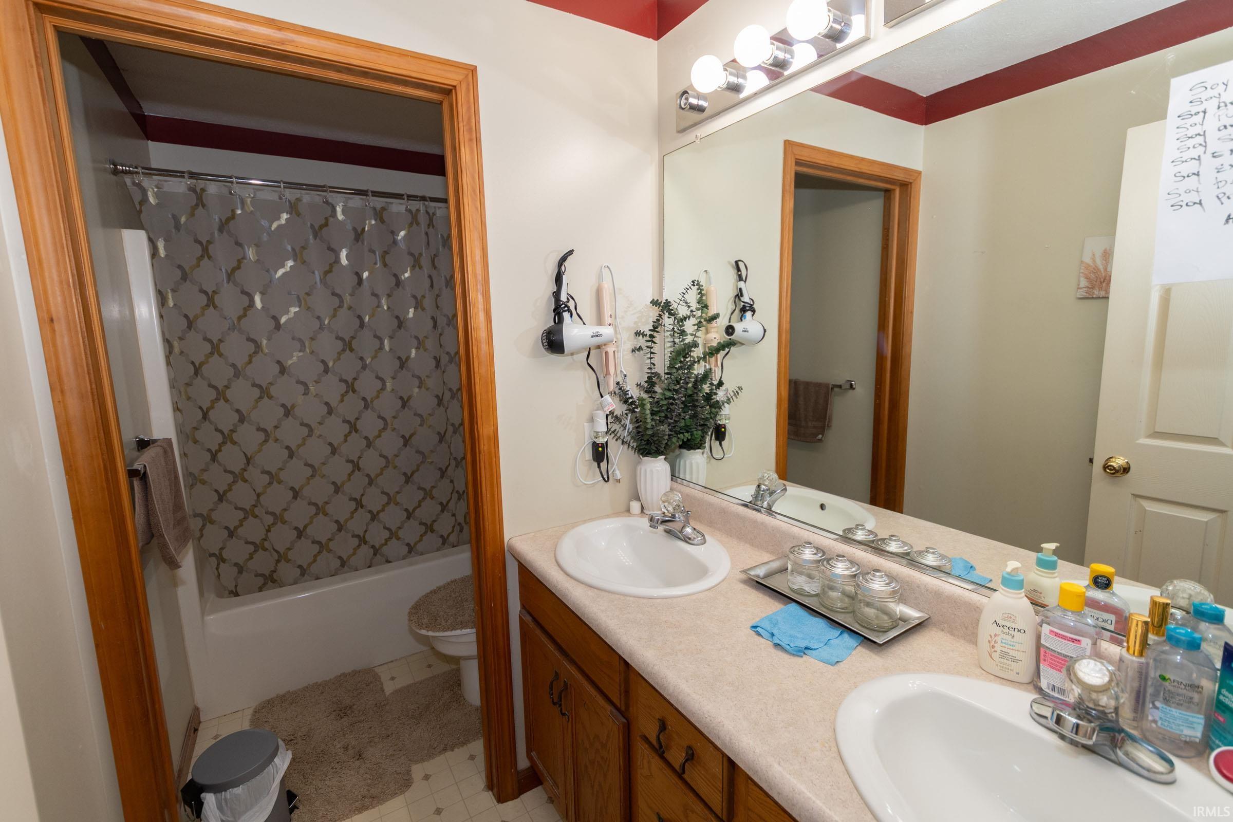 Bathroom featuring a dual-sink vanity with a light-toned countertop, wood-finish cabinetry, and a full-width mirror with a four-bulb vanity light