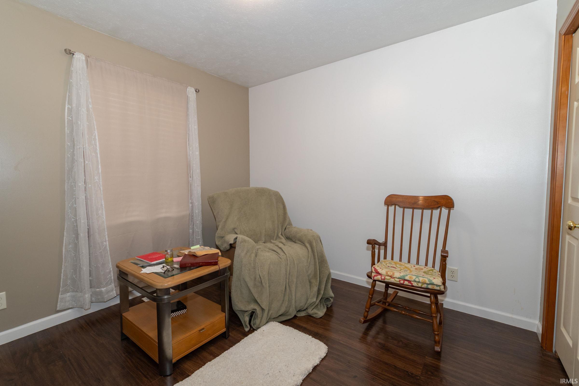 Room featuring wood-finish flooring, white baseboards, and a window with sheer curtains