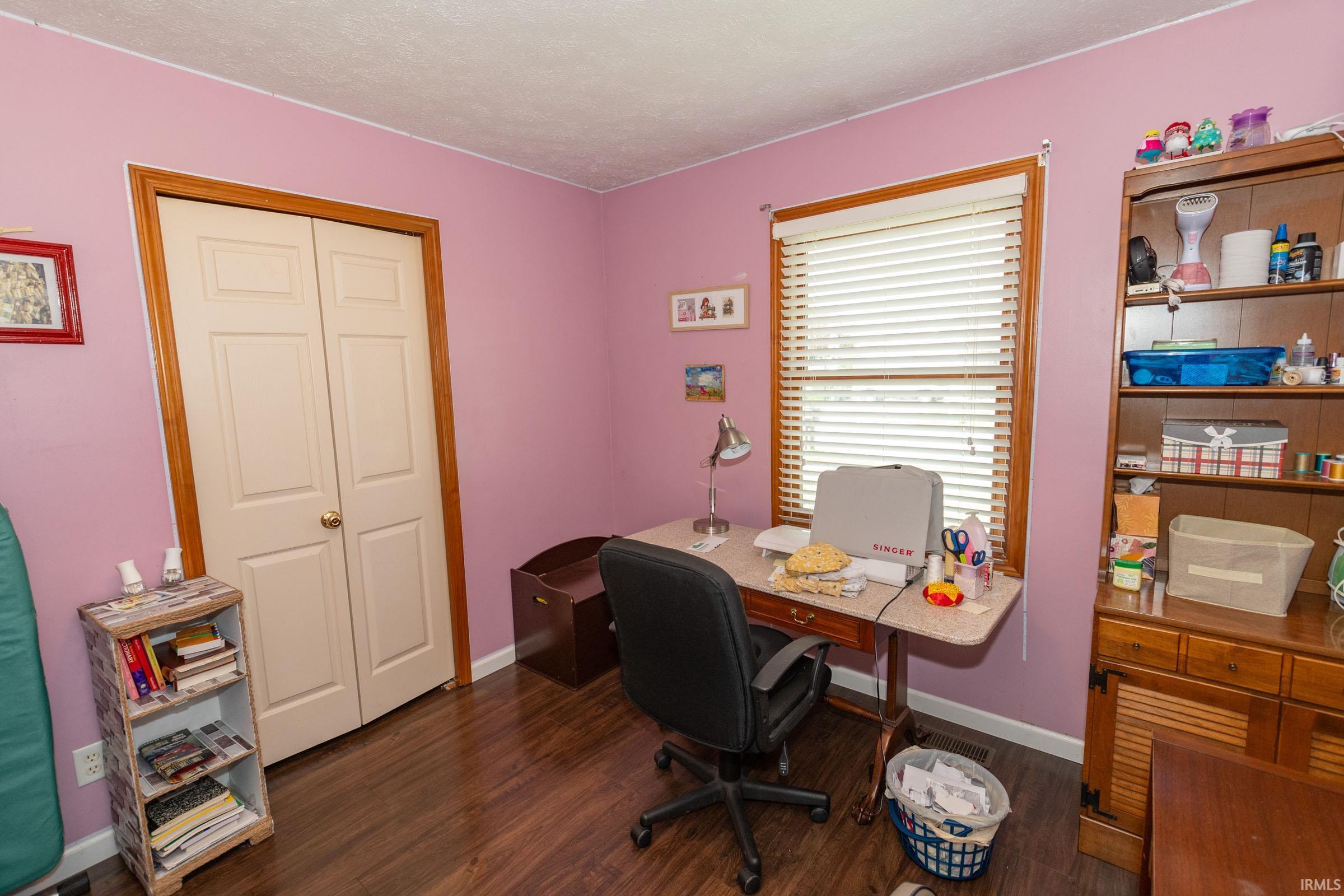 Room featuring wood-finish flooring, a window with blinds, and a built-in closet with bi-fold doors