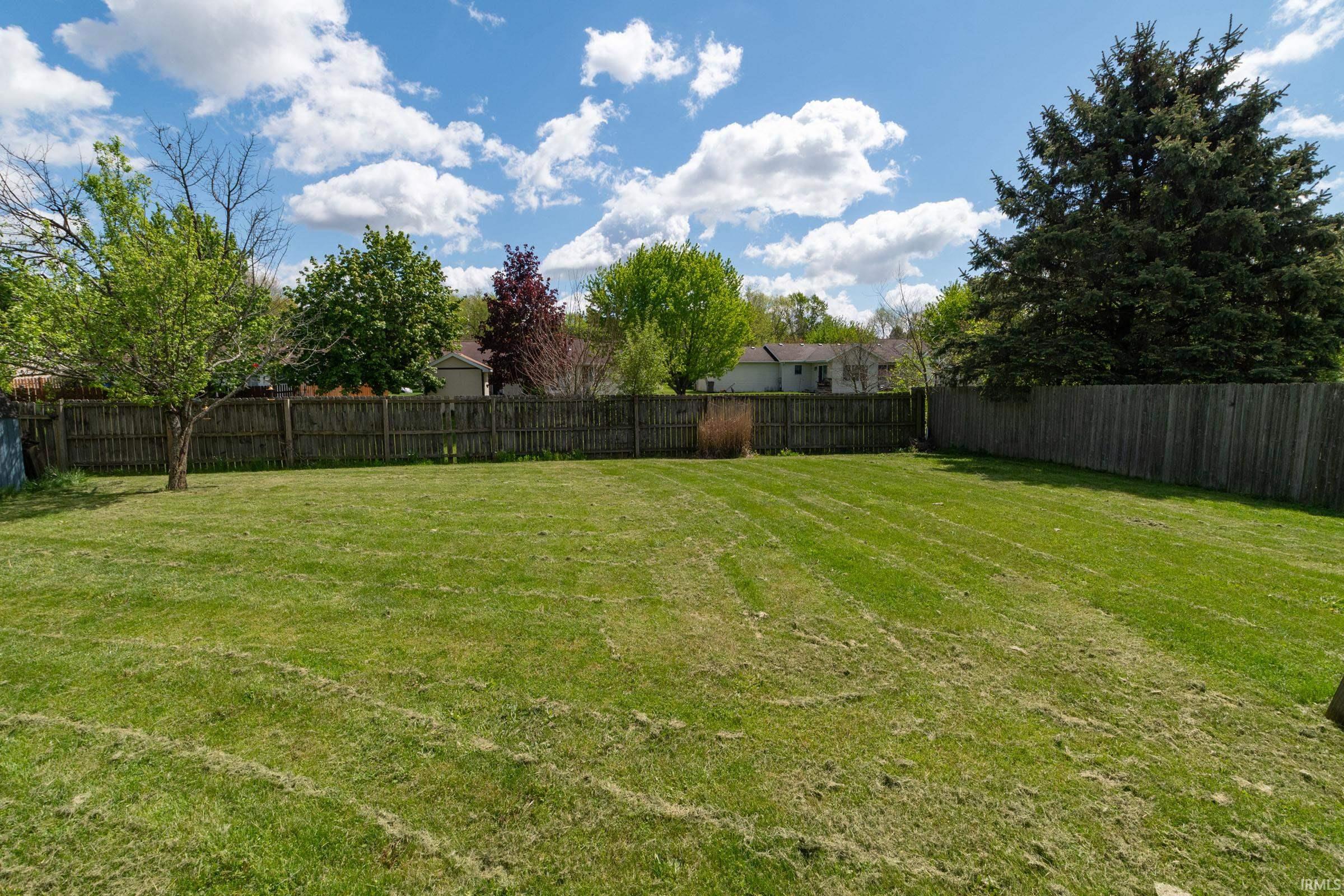 Spacious backyard featuring a full perimeter wood fence, mature evergreen tree, and a deciduous tree