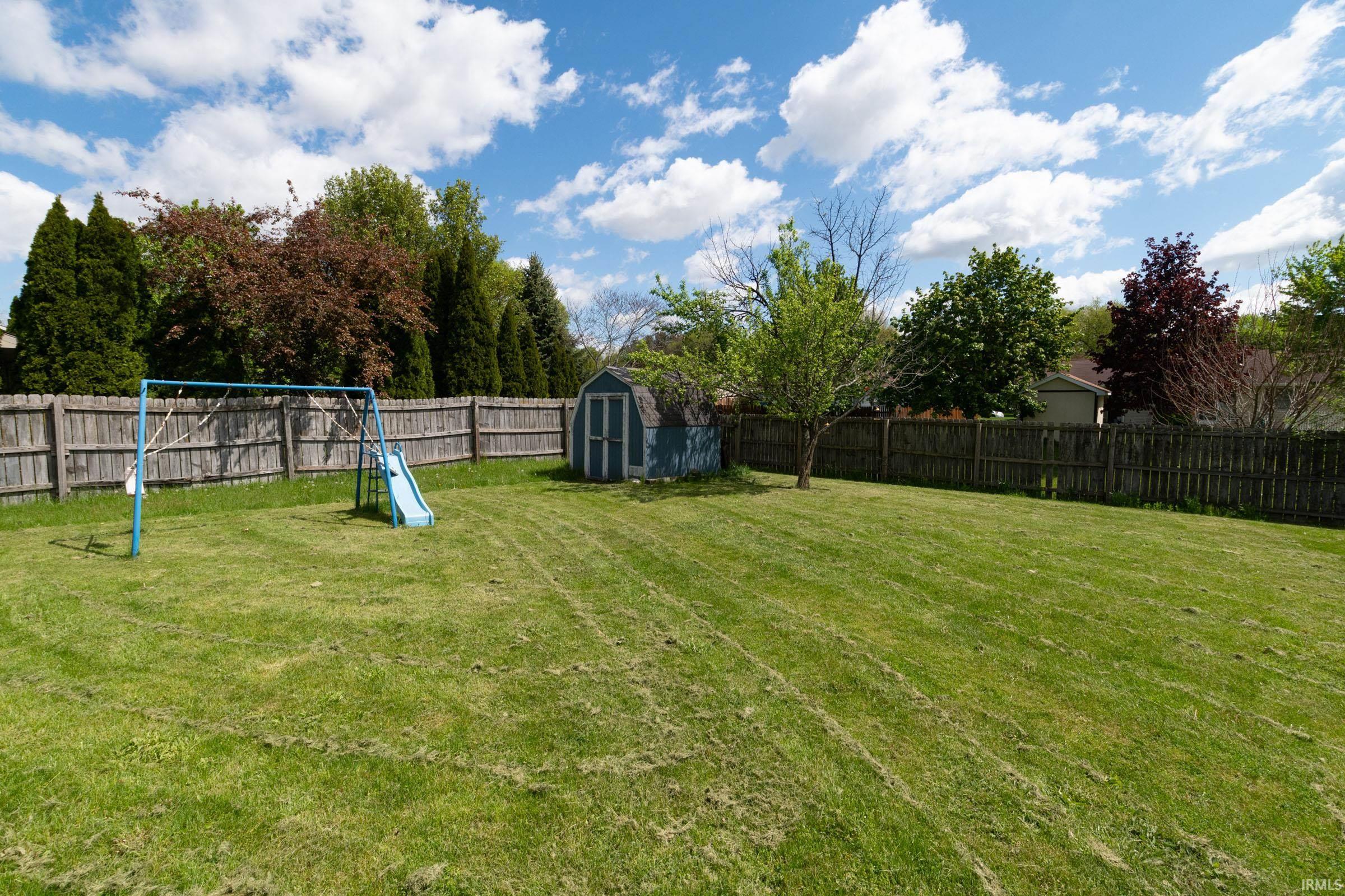 Expansive green lawn with a wooden privacy fence, mature trees, and a functional storage shed