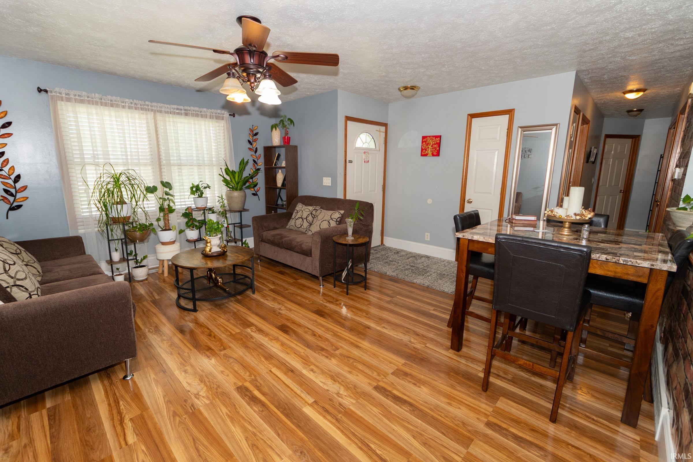 Open-concept living space featuring wood-finish flooring, a ceiling fan with integrated lighting, and a dining area with a stone-look countertop