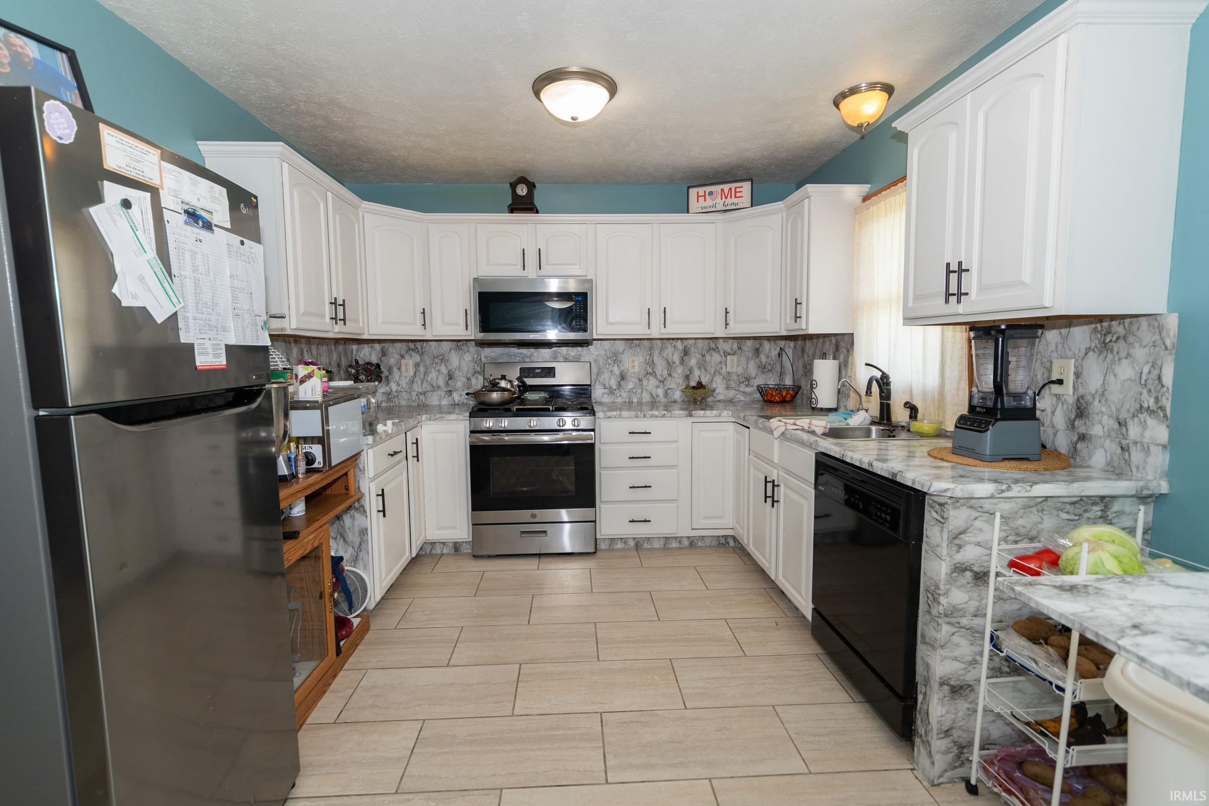 U-shaped kitchen featuring white cabinetry, gray patterned countertops and backsplash, stainless steel appliances, and light-toned tile flooring