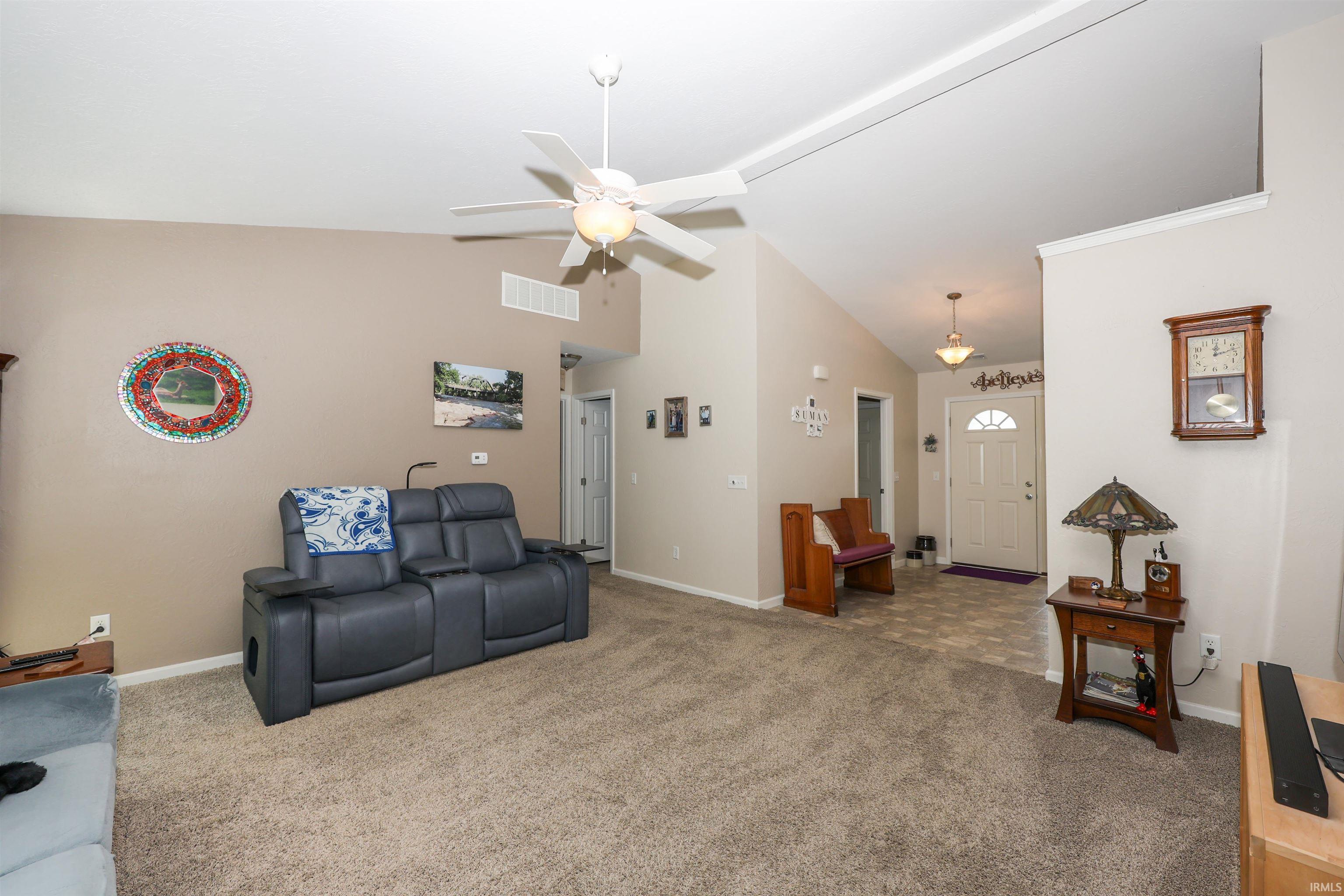 Vaulted ceiling living area featuring a ceiling fan, recessed wall niche, and carpet flooring