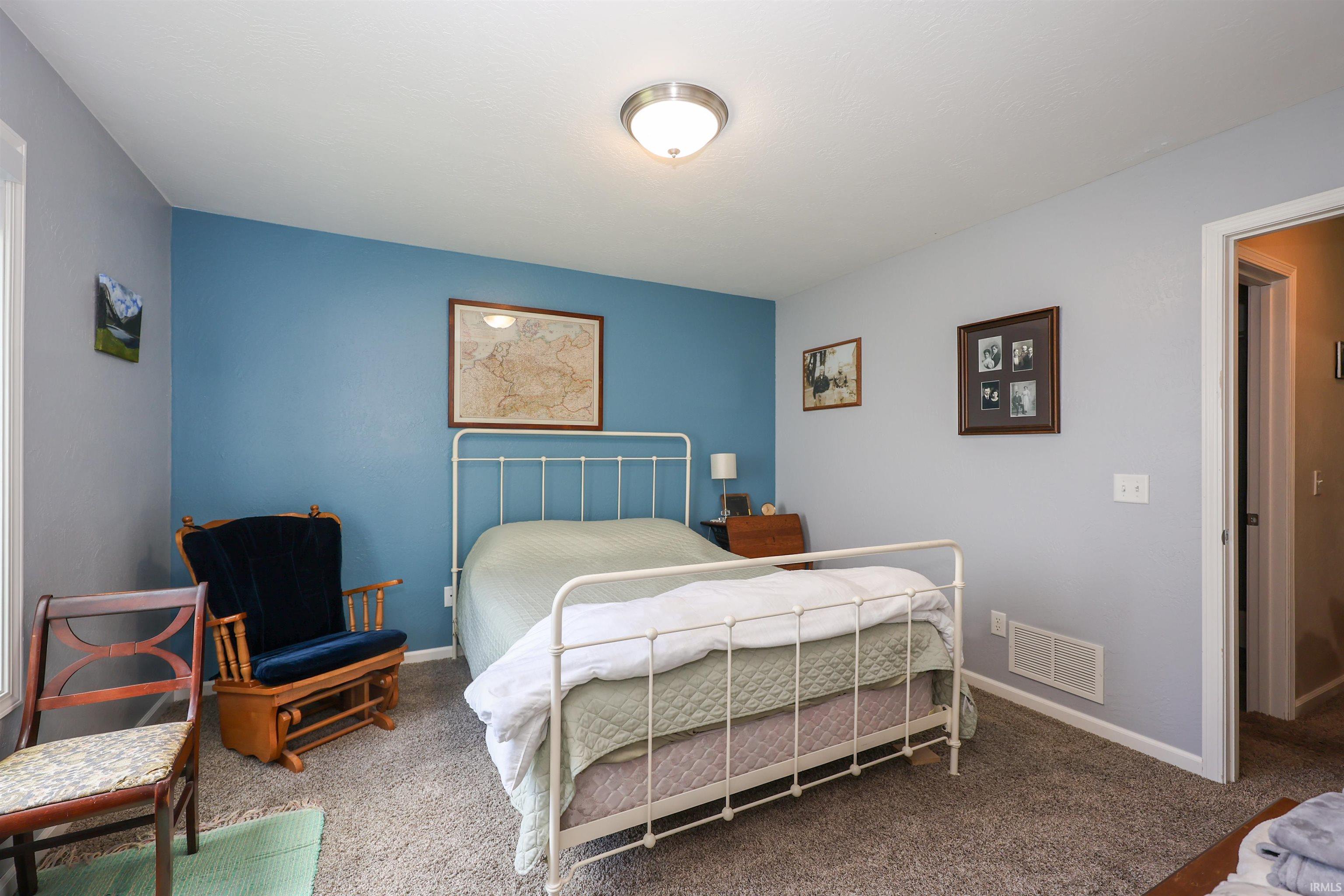 Bedroom featuring light gray walls with a contrasting blue accent wall, carpeted flooring, and a flush-mount ceiling light fixture