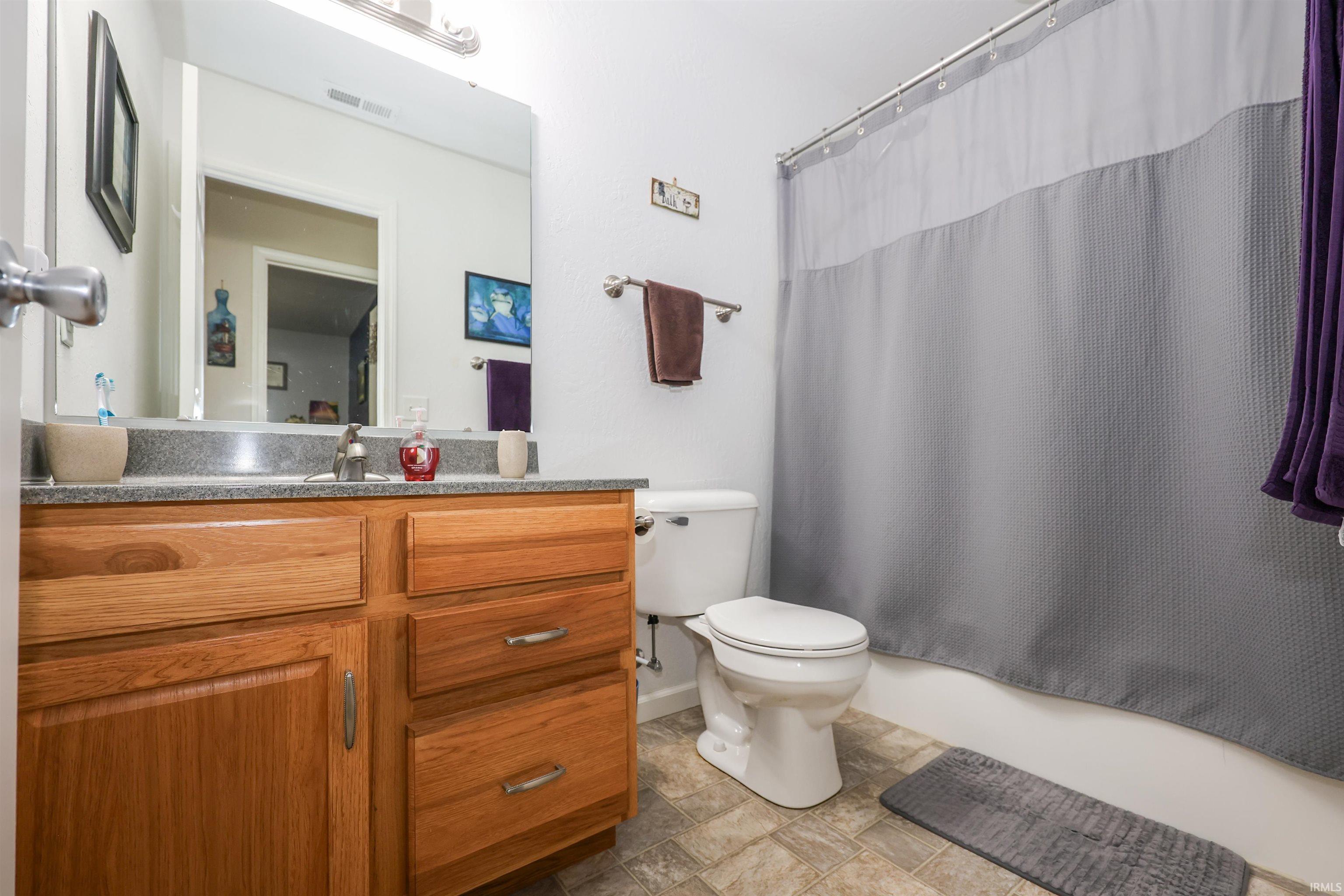 Bathroom featuring a light wood-finish vanity with a gray countertop, an integrated sink with a chrome faucet, a wall-mounted mirror, and a white toilet
