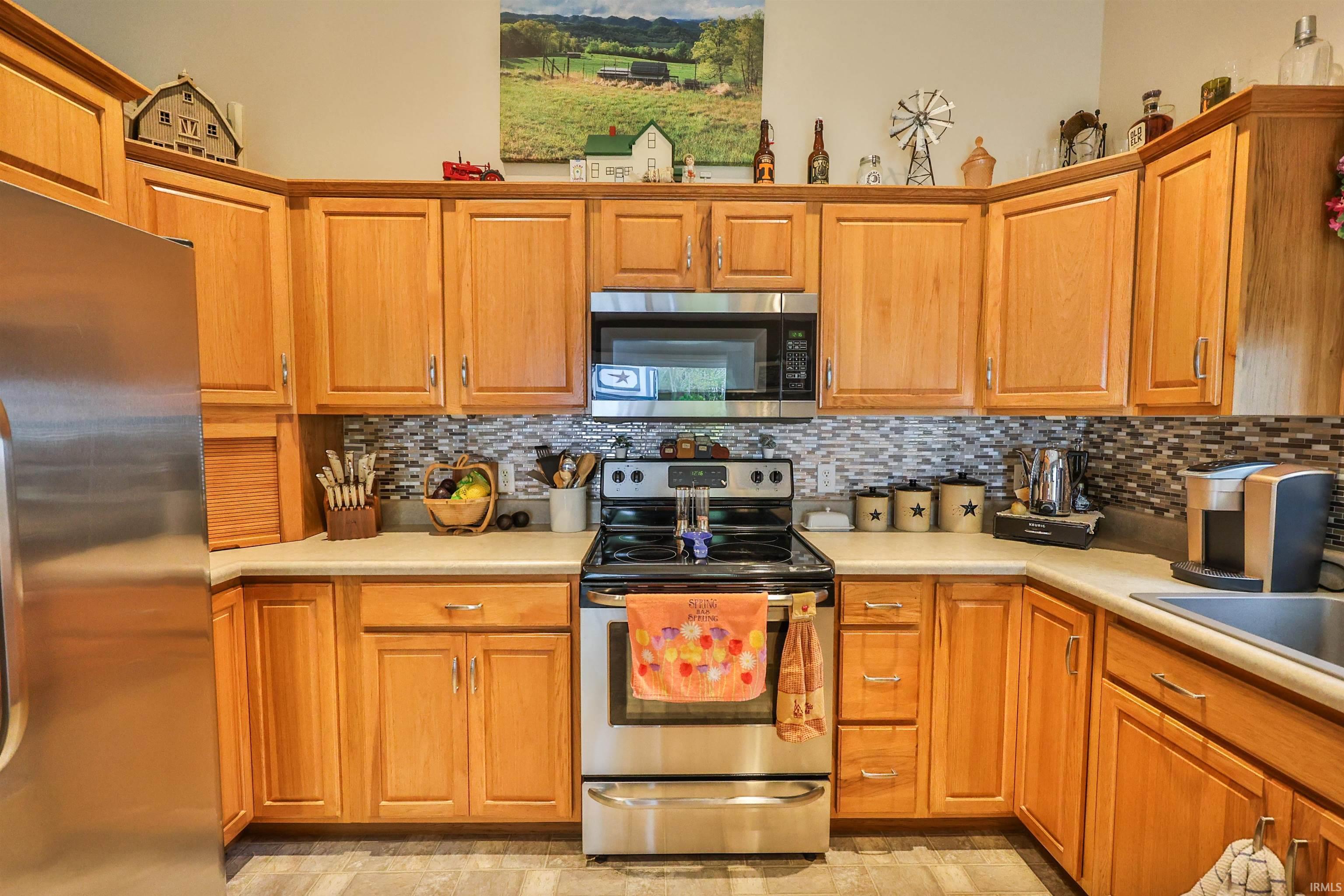 Kitchen featuring stainless steel appliances, light wood cabinetry, a mosaic tile backsplash, and a double basin sink
