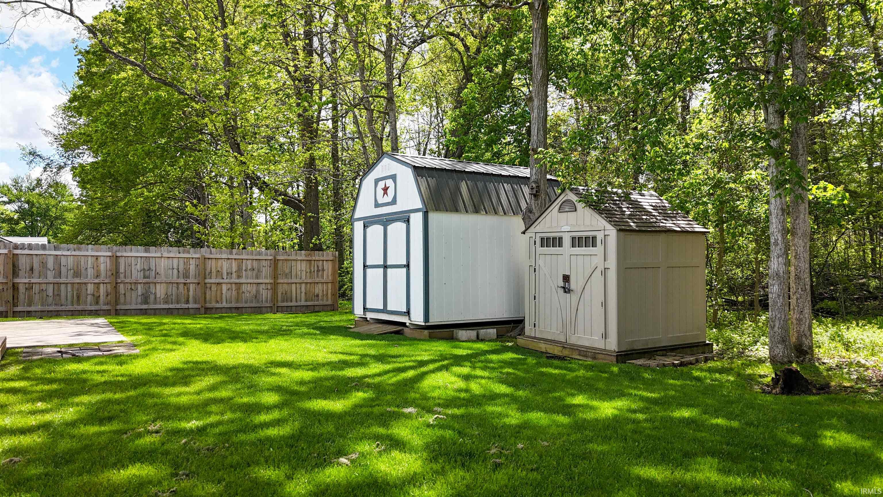 Expansive green lawn featuring two storage sheds, mature trees, and a wooden privacy fence