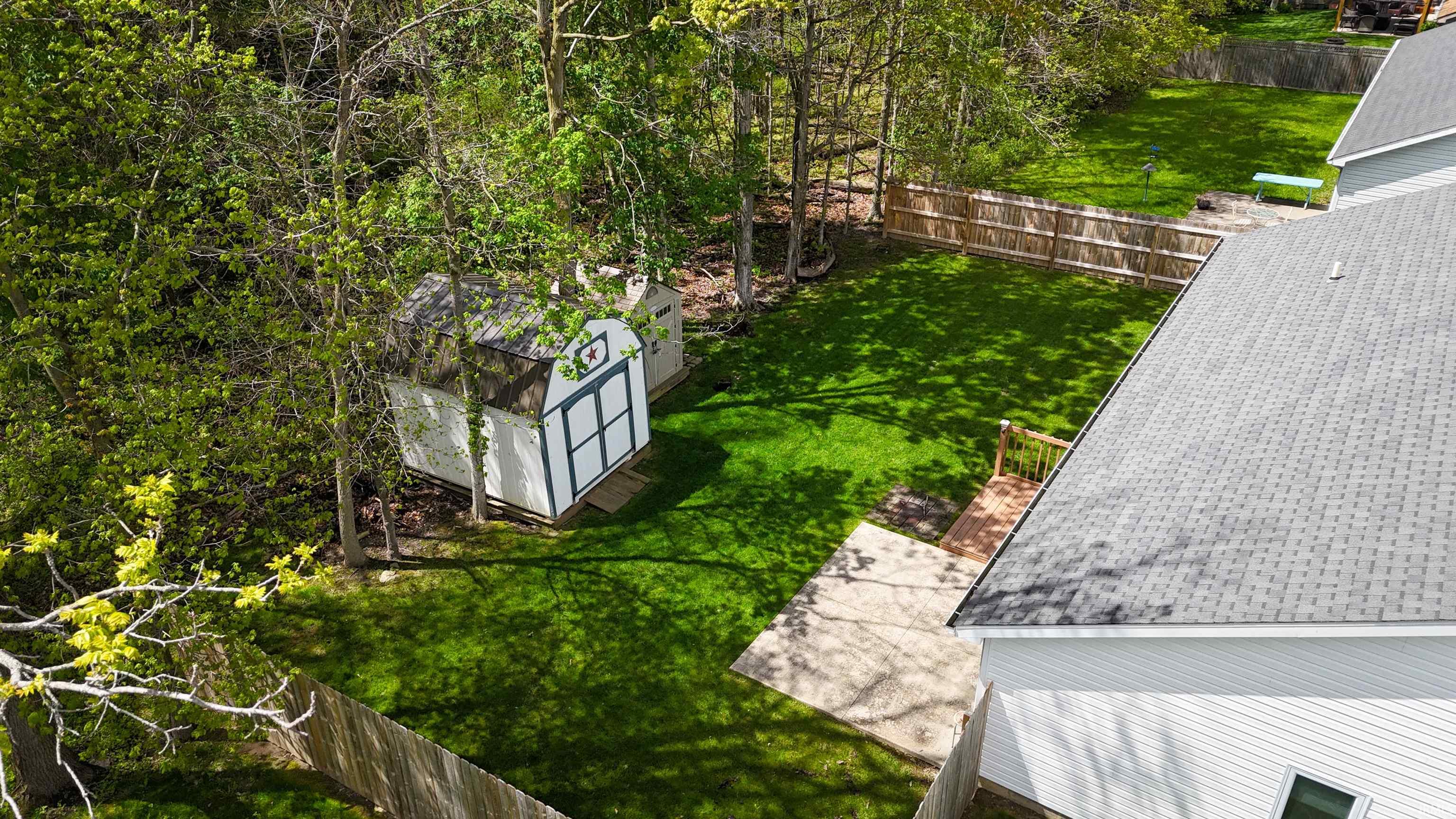 Expansive backyard featuring a green lawn, wood privacy fencing, two storage sheds, a small wooden deck, and concrete patio