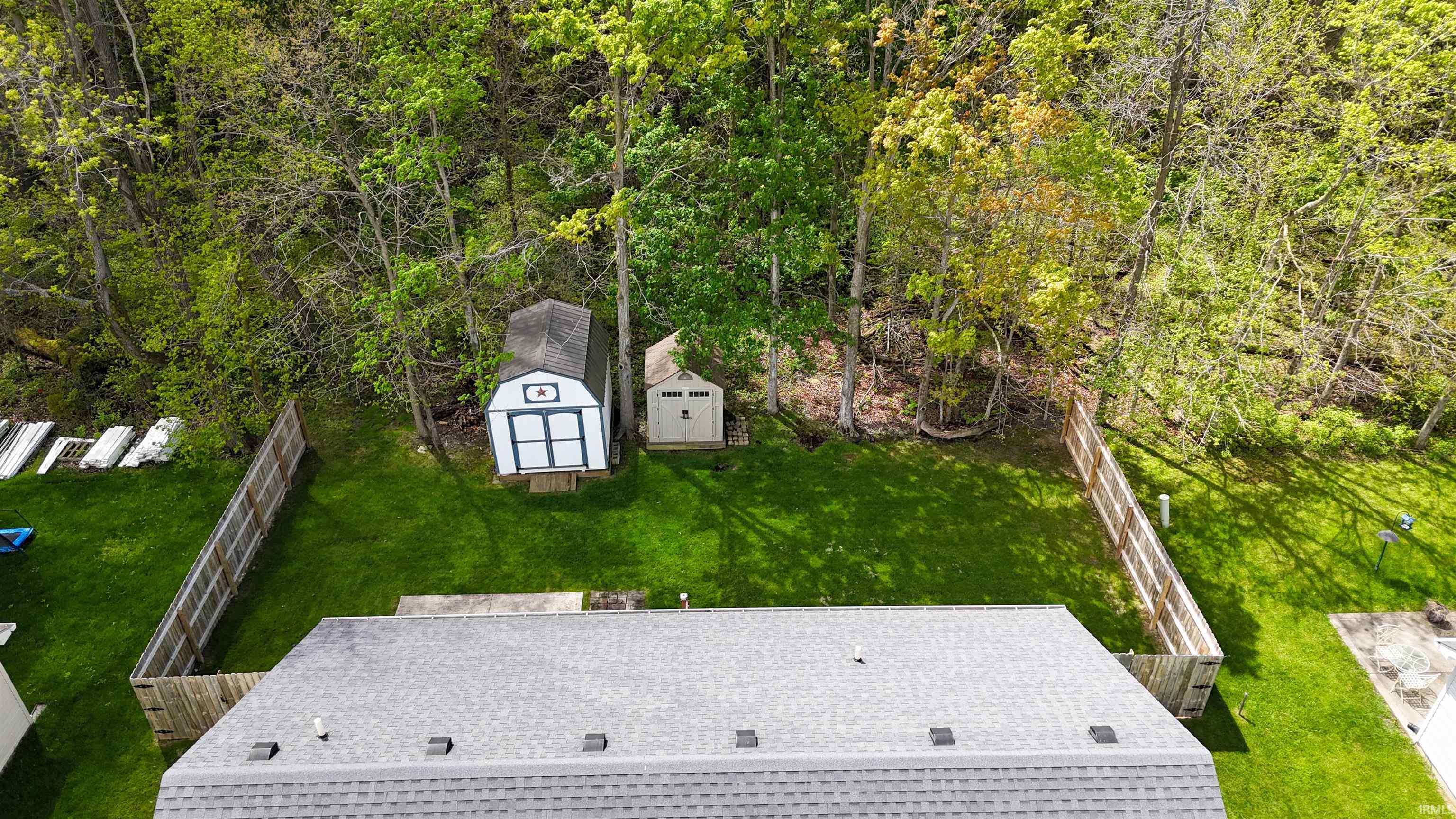 Fenced backyard with mature trees, offering two storage sheds and a manicured lawn