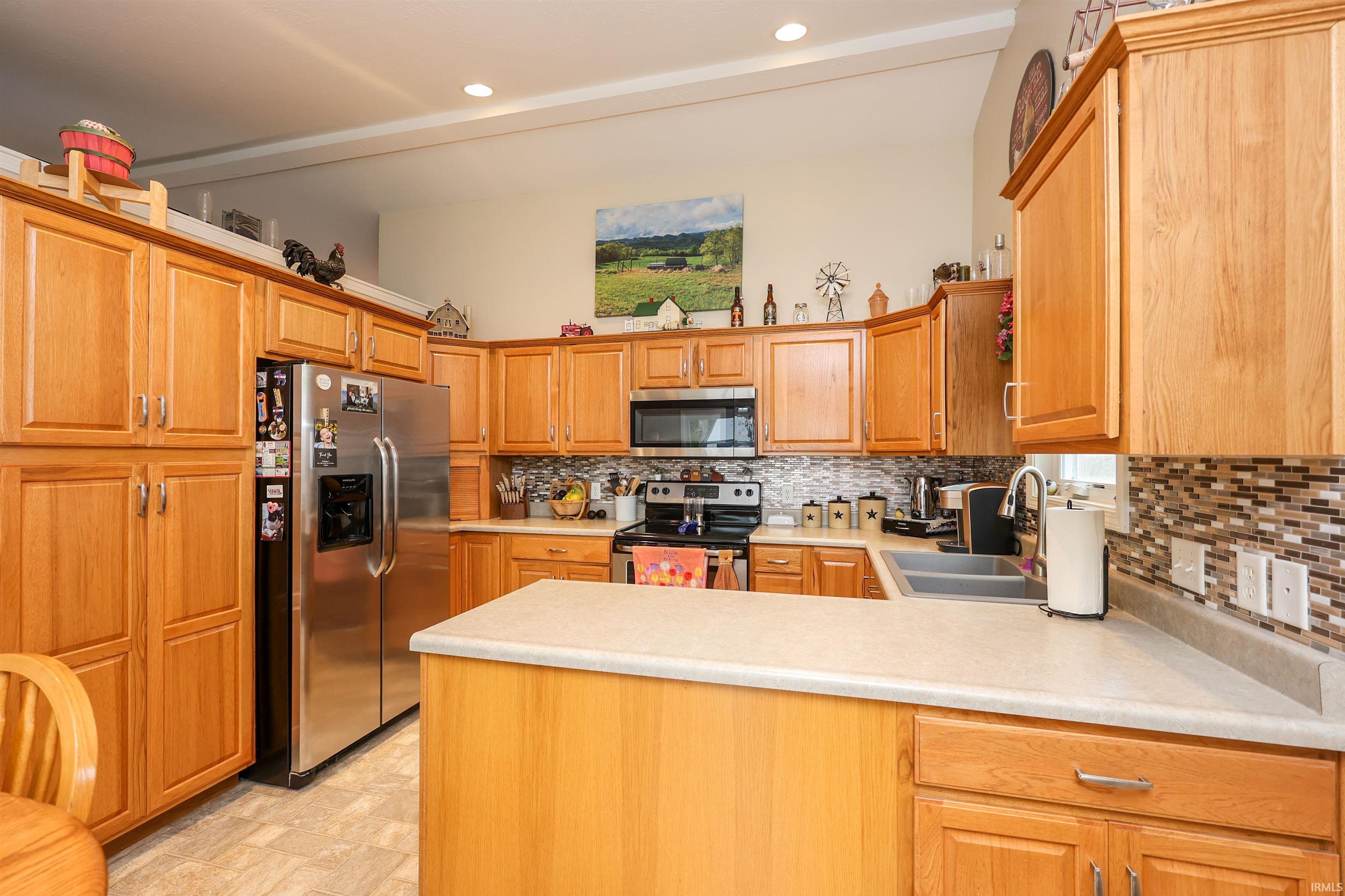 Kitchen featuring wood-finish cabinetry, stainless steel refrigerator, built-in microwave, tile backsplash, and light-toned countertops