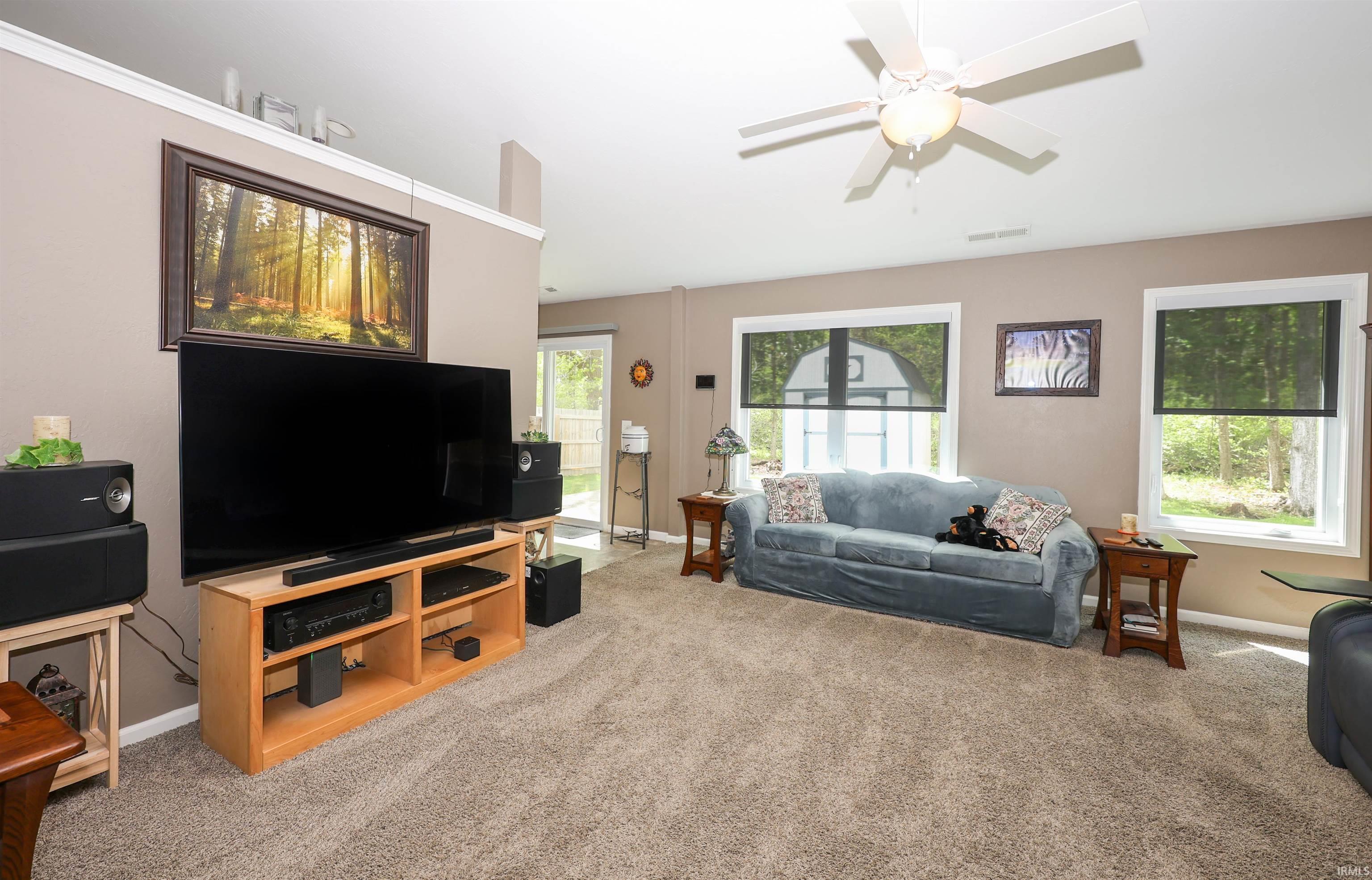 Carpeted living area featuring a ceiling fan with light, recessed wall niche, and light-colored walls