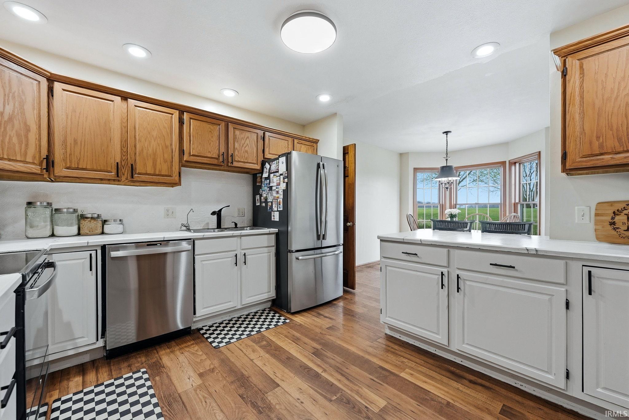 Kitchen featuring wood-finish flooring, white countertops, stainless steel appliances, upper wood cabinetry, and lower white cabinetry
