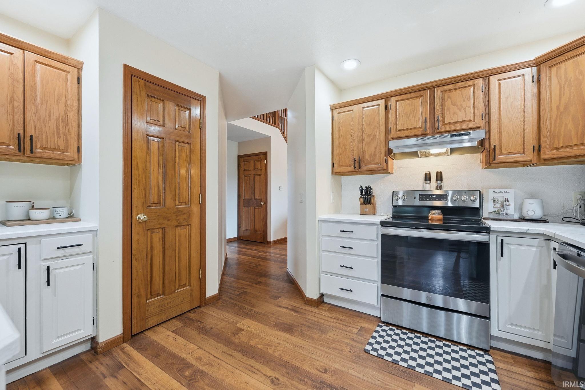 Kitchen featuring wood-finish flooring, two-tone cabinetry with white base cabinets and wood-finish upper cabinets, white countertops, and a stainless steel range