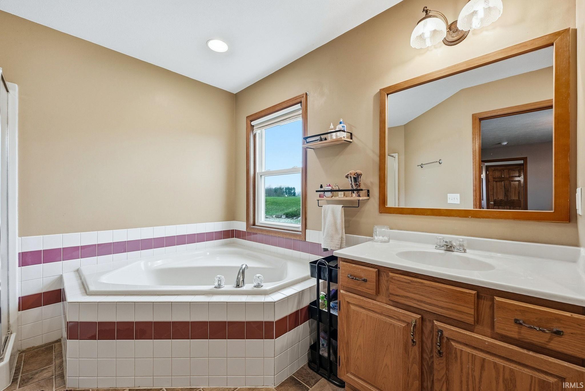 Bathroom featuring a corner soaking tub with tile surround, a single vanity with wood-finish cabinetry, a white countertop, and an integrated sink