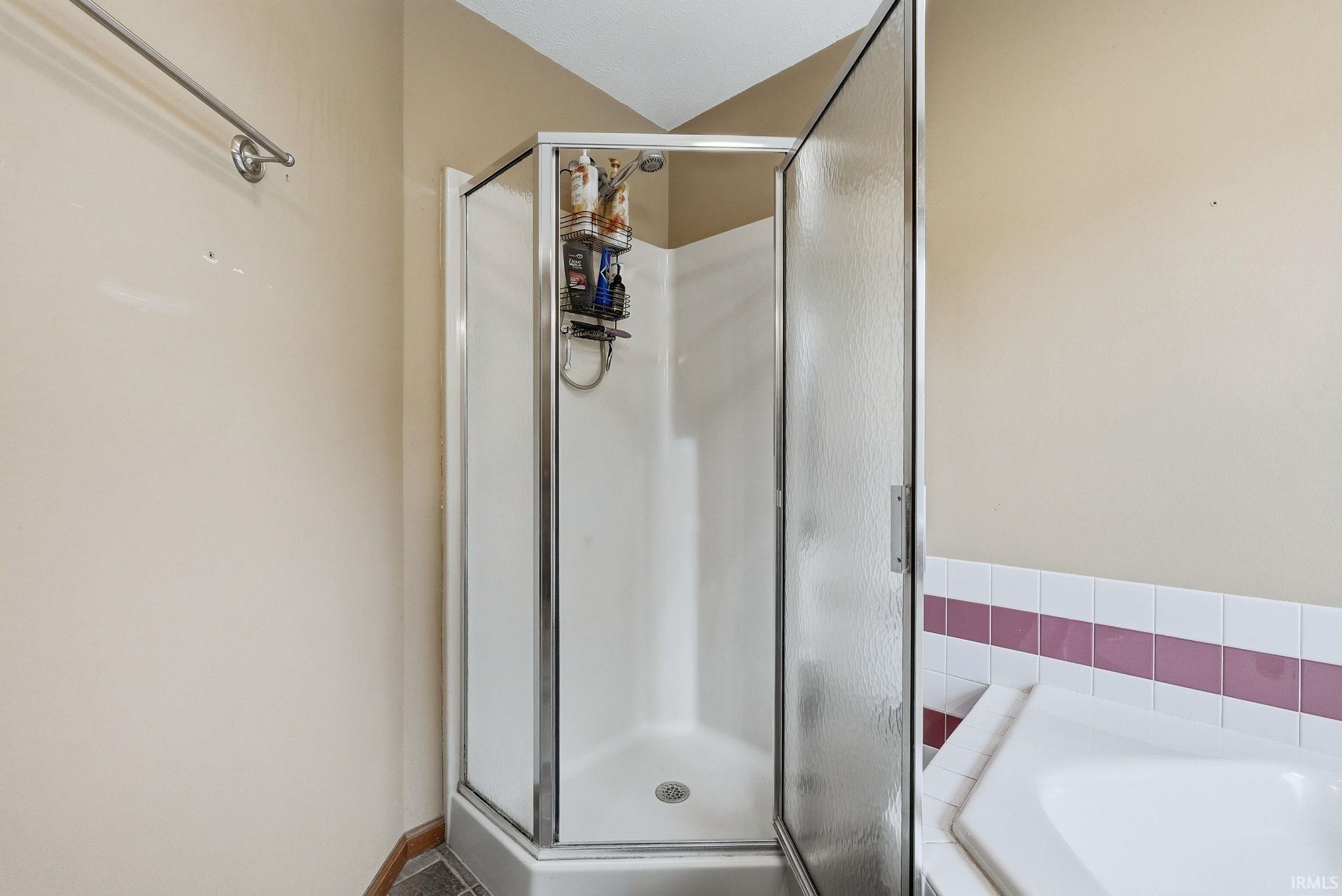 Corner shower enclosure with clear glass door, white shower pan, white tile surround, and a chrome shower fixture
