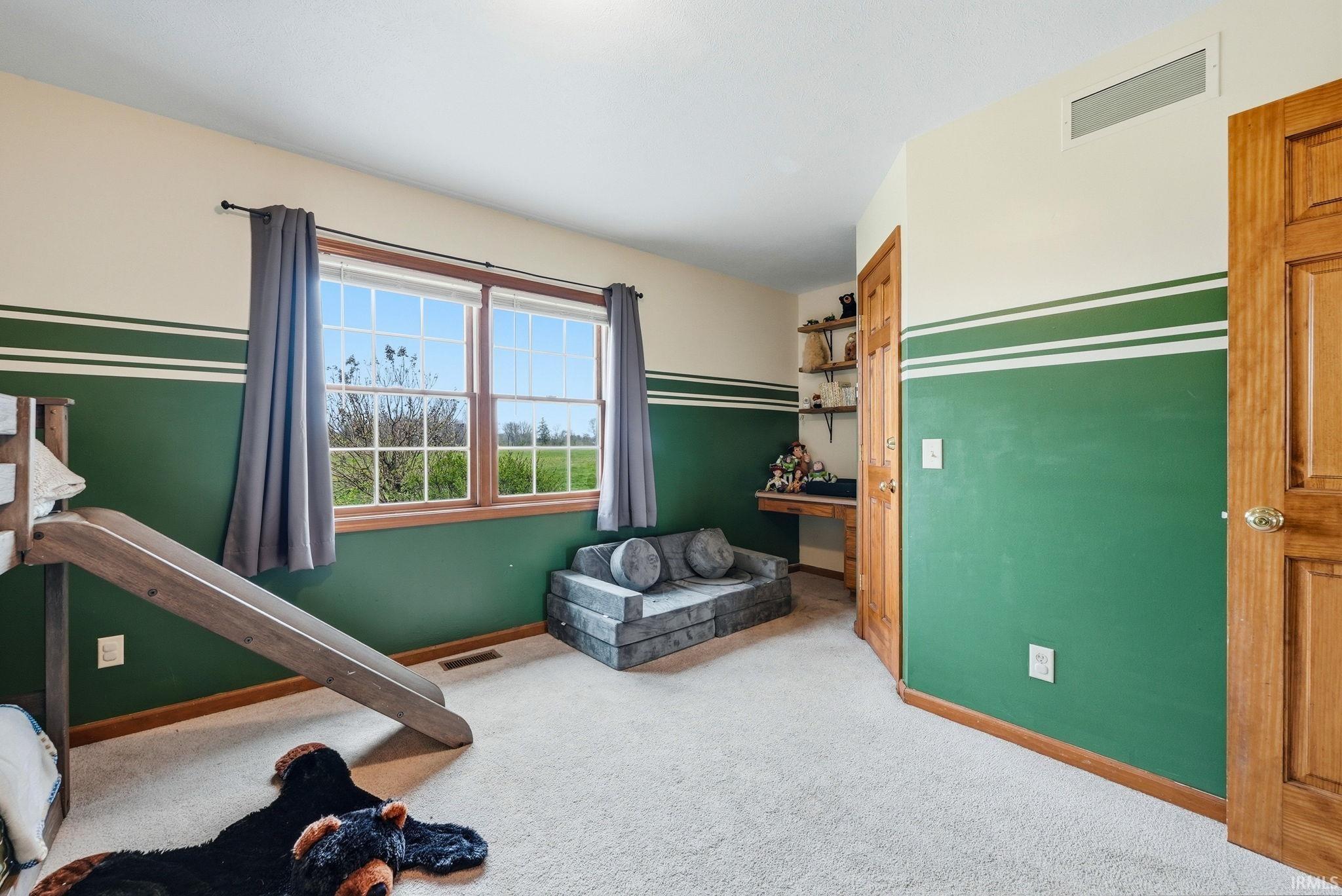 Spacious room featuring light-toned carpet flooring, two double-hung windows with wood trim, and a built-in desk with shelving