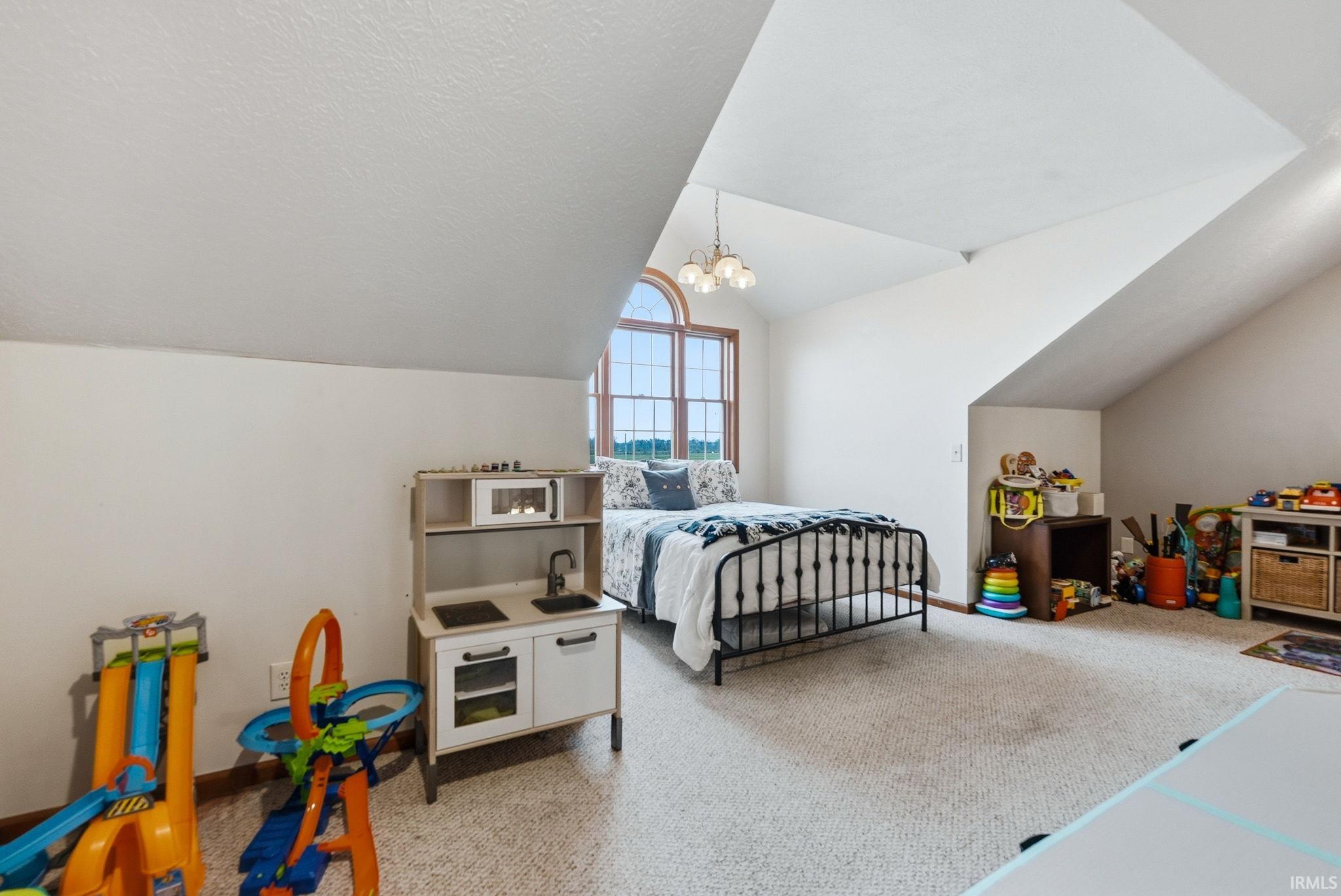 Carpeted room featuring a large arched window with grid details, a sloped ceiling, and a multi-light ceiling fixture