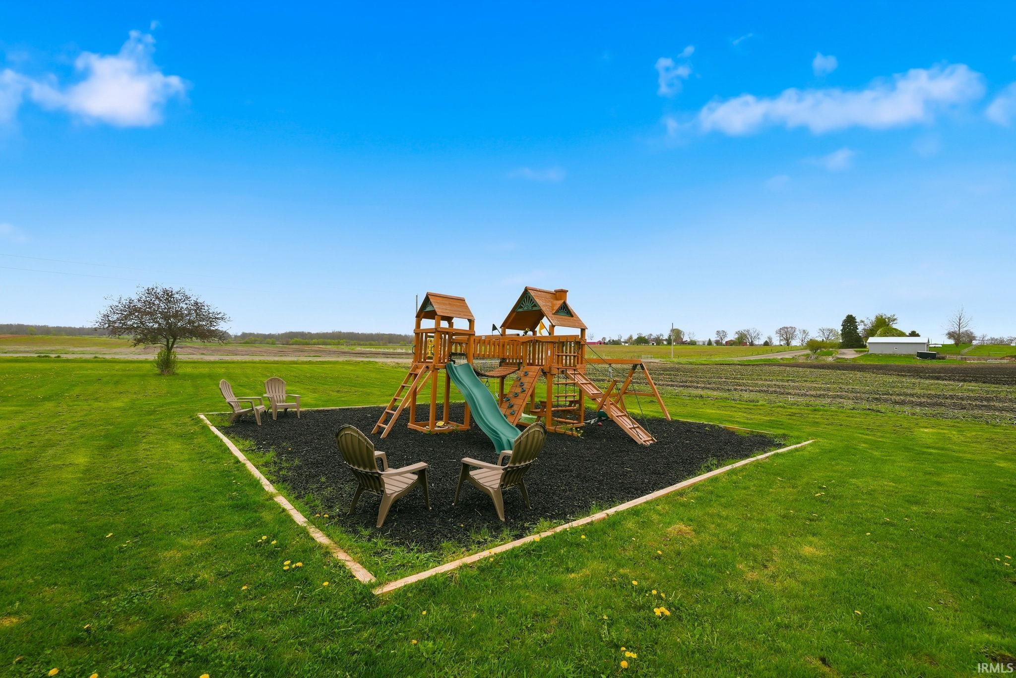 Expansive green lawn featuring a wooden playset with slide and swings, surrounded by a dark ground covering