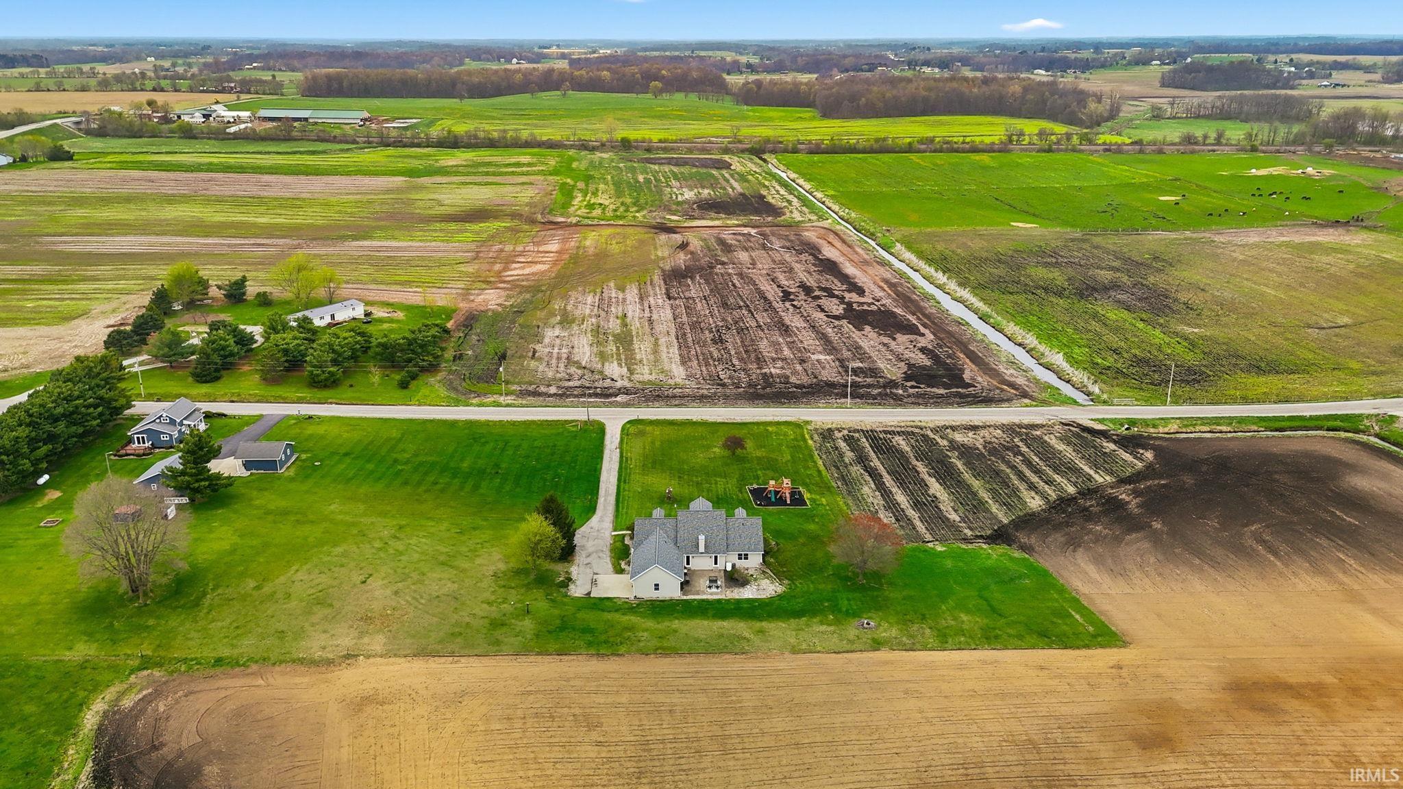 Expansive agricultural land parcel featuring a detached two-story residence with a light-colored exterior and a dark roof