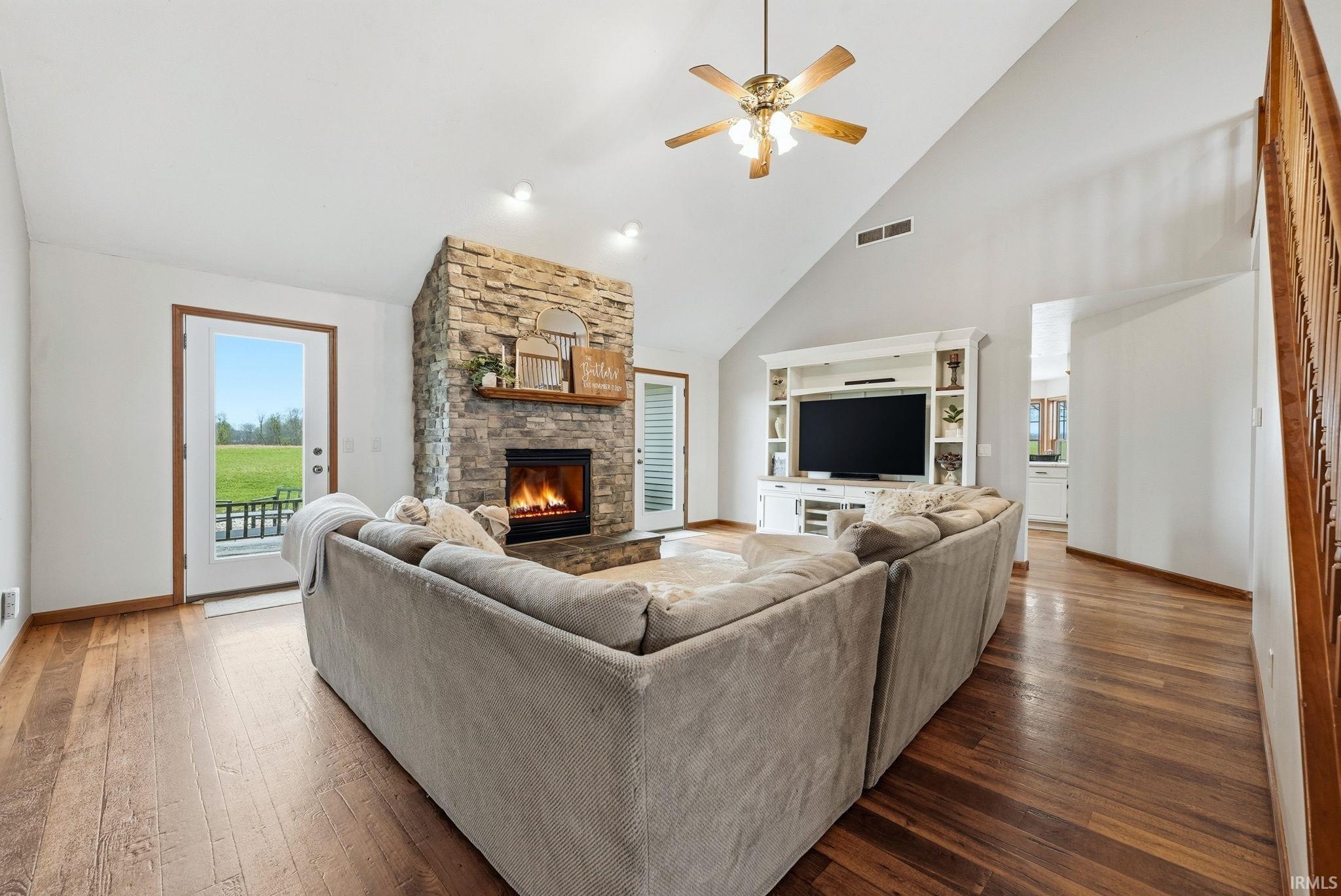 Vaulted ceiling living room featuring a stone-clad fireplace with wood mantel, wood-finish flooring, and a built-in entertainment center