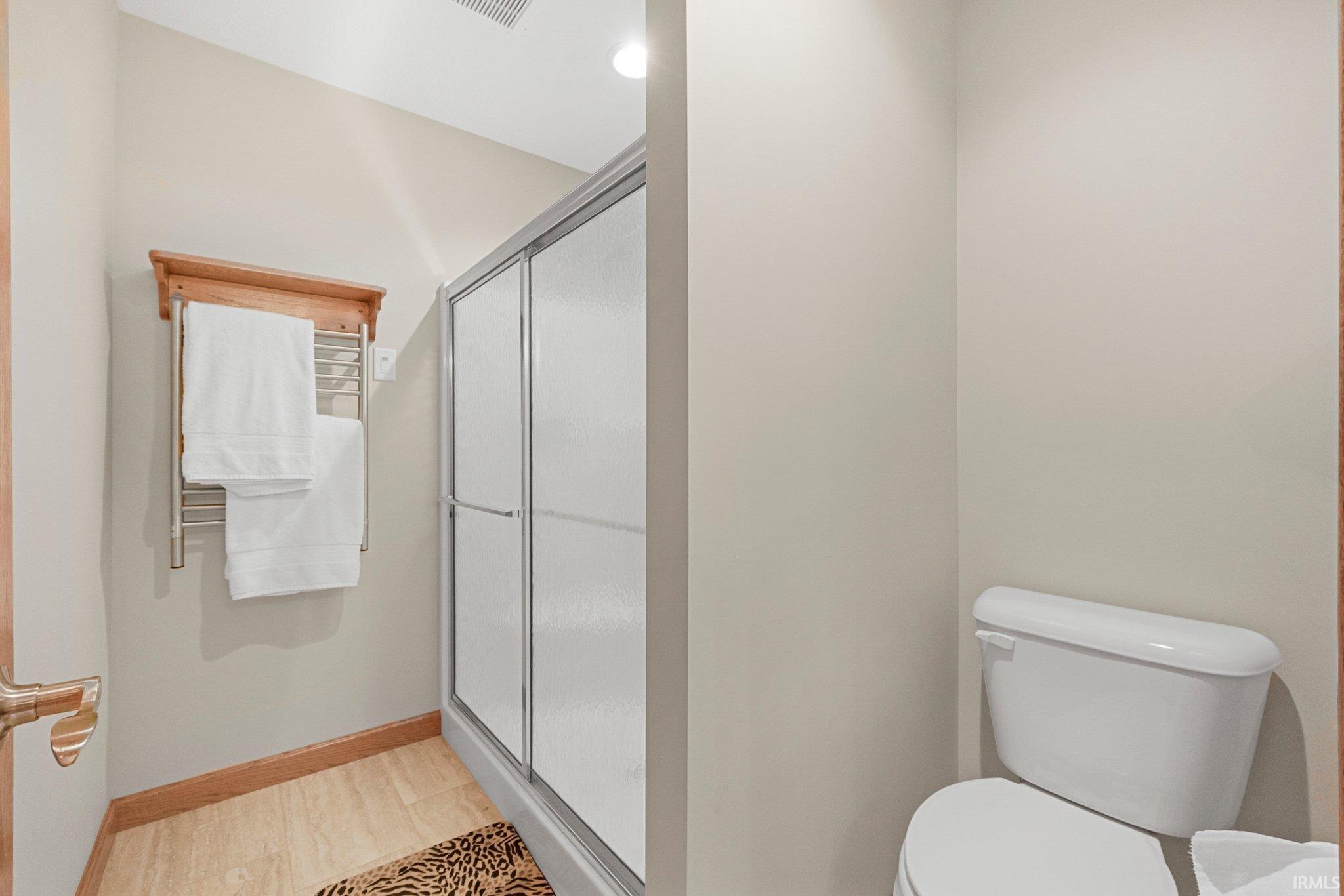 Shower enclosure with sliding frosted glass doors, a built-in towel warmer, and a white toilet