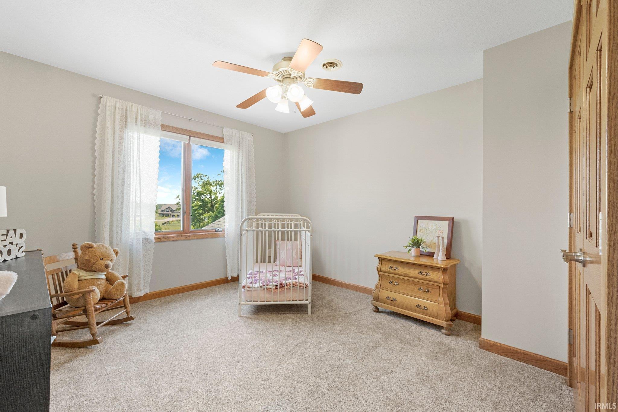 Carpeted room featuring light-toned walls, a double window with wood-finish trim, a ceiling fan with integrated lighting, and a paneled wood-finish door
