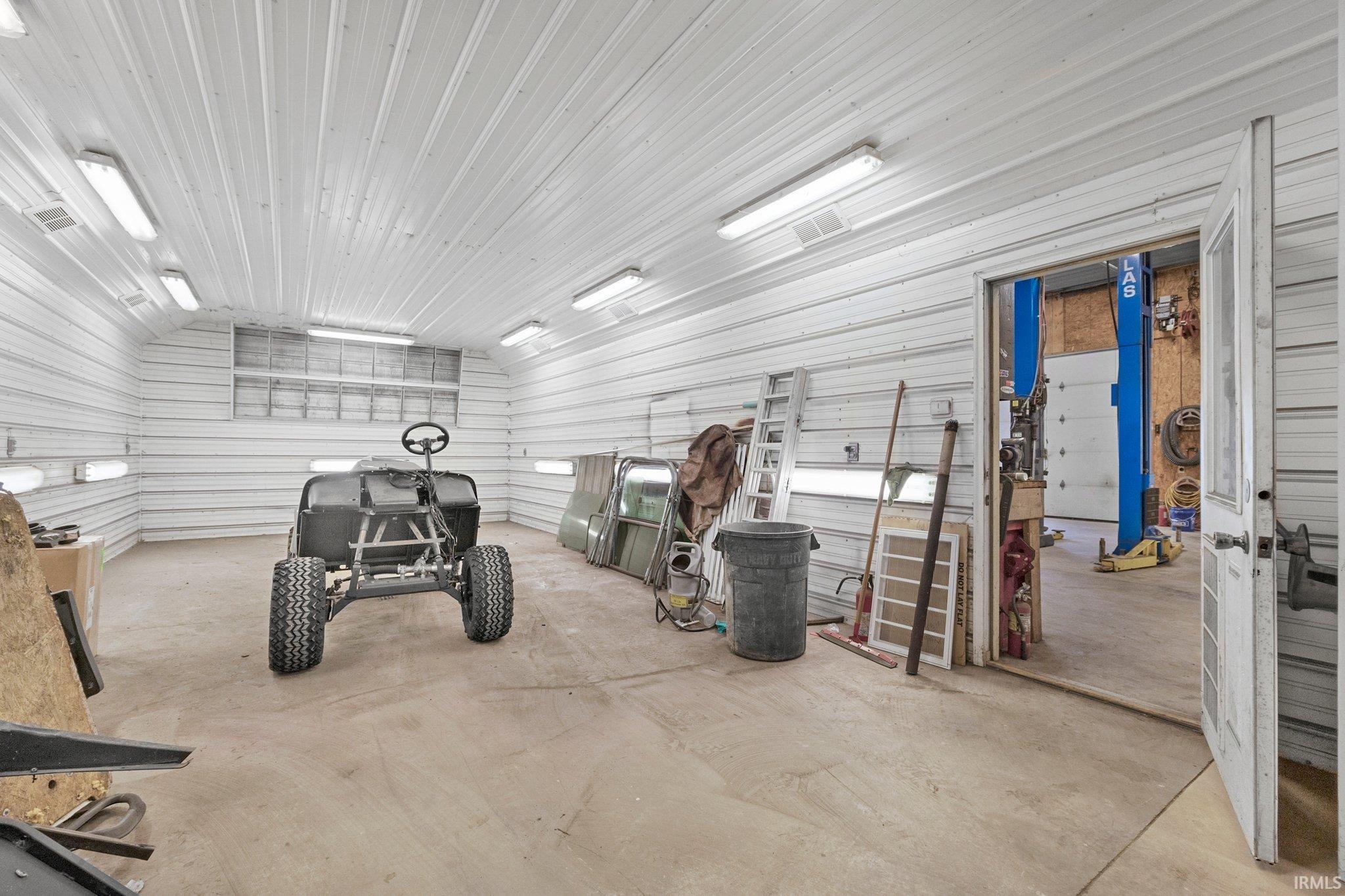Spacious workshop featuring corrugated metal walls and ceiling, concrete flooring, and multiple fluorescent light fixtures