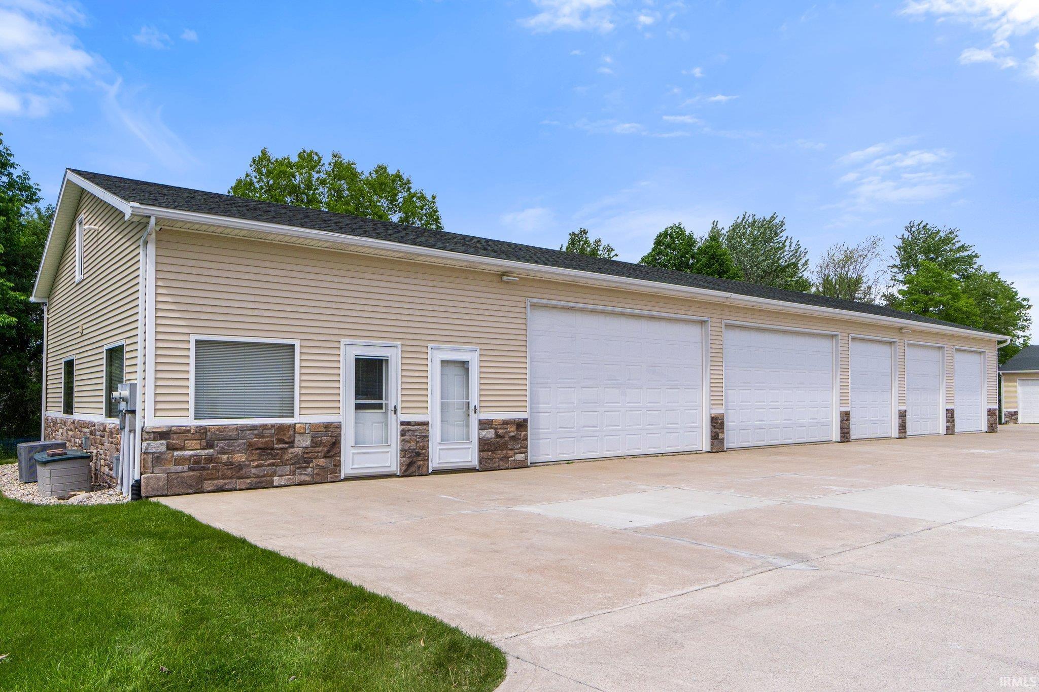 Spacious garage structure featuring five individual overhead doors, durable concrete driveway, stone-look foundation, and tan horizontal siding