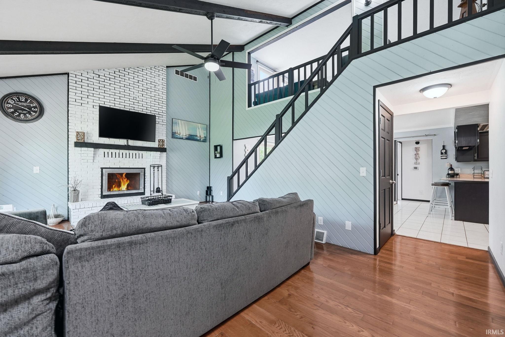 Living area featuring a white brick fireplace with a mantle, wood-finish flooring, and a black ceiling fan