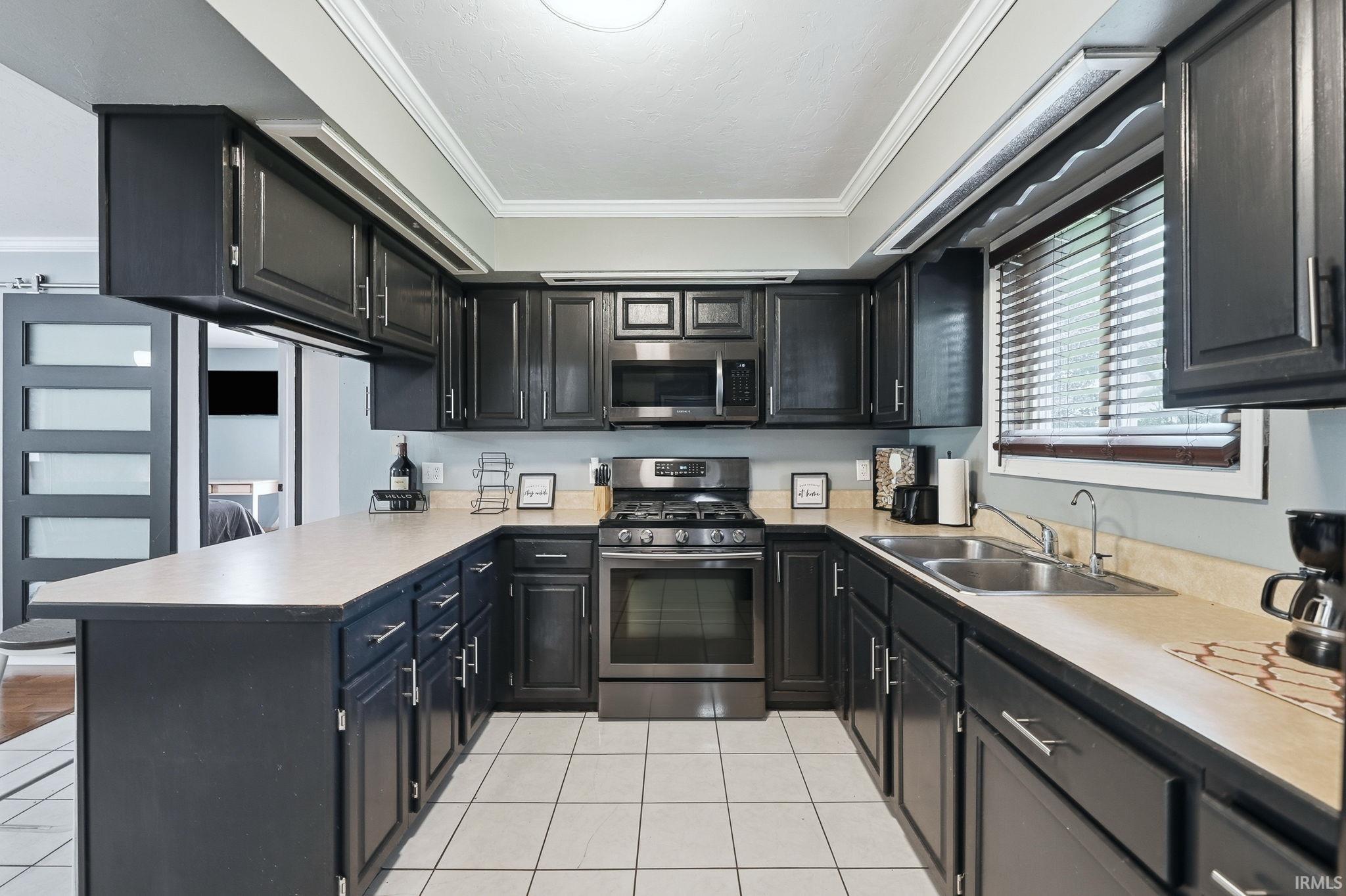 U-shaped kitchen featuring dark cabinetry, stainless steel appliances, a double basin sink, light-toned countertops, and white square floor tiles