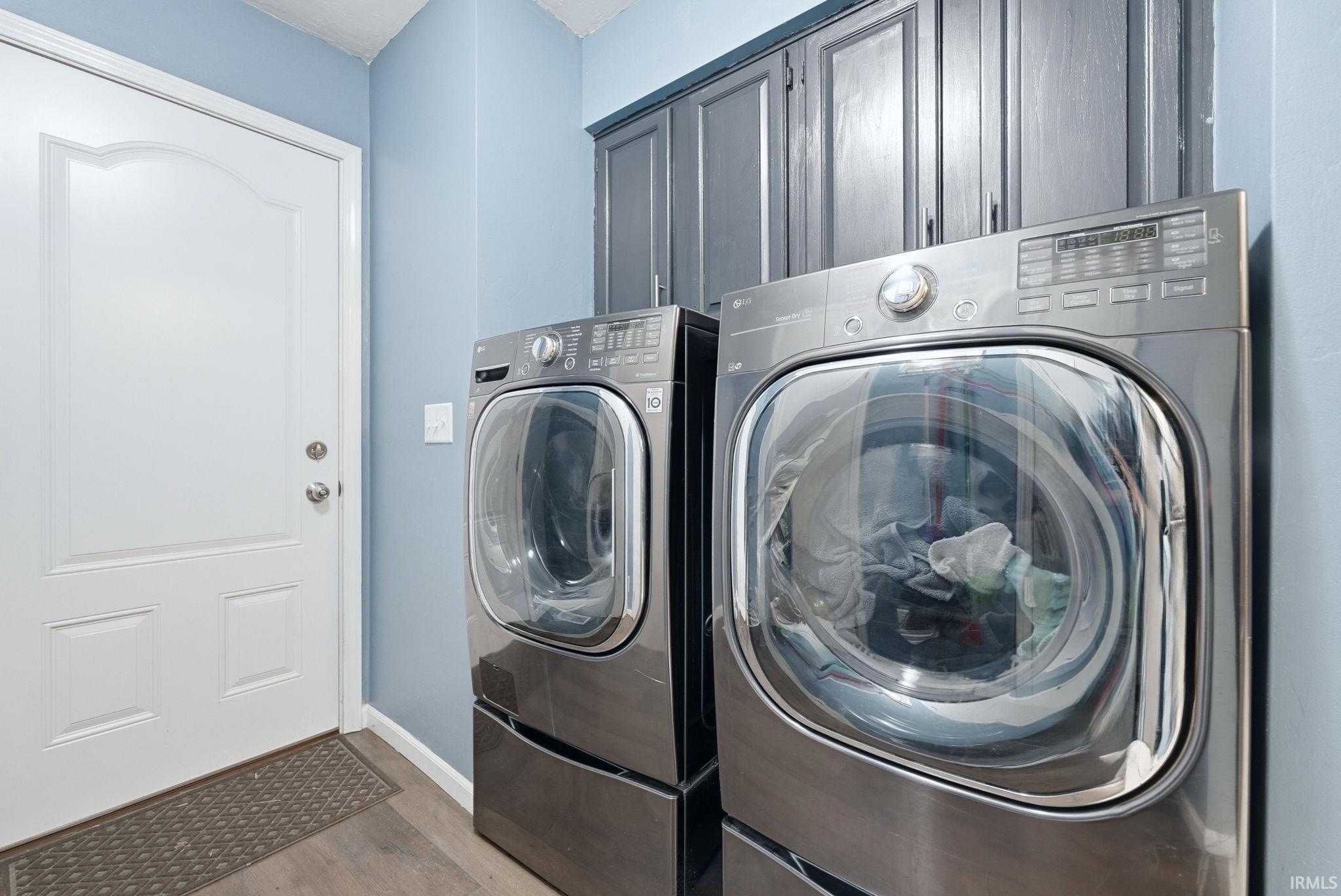Dedicated laundry area featuring front-loading appliances, overhead cabinetry, and wood-finish flooring