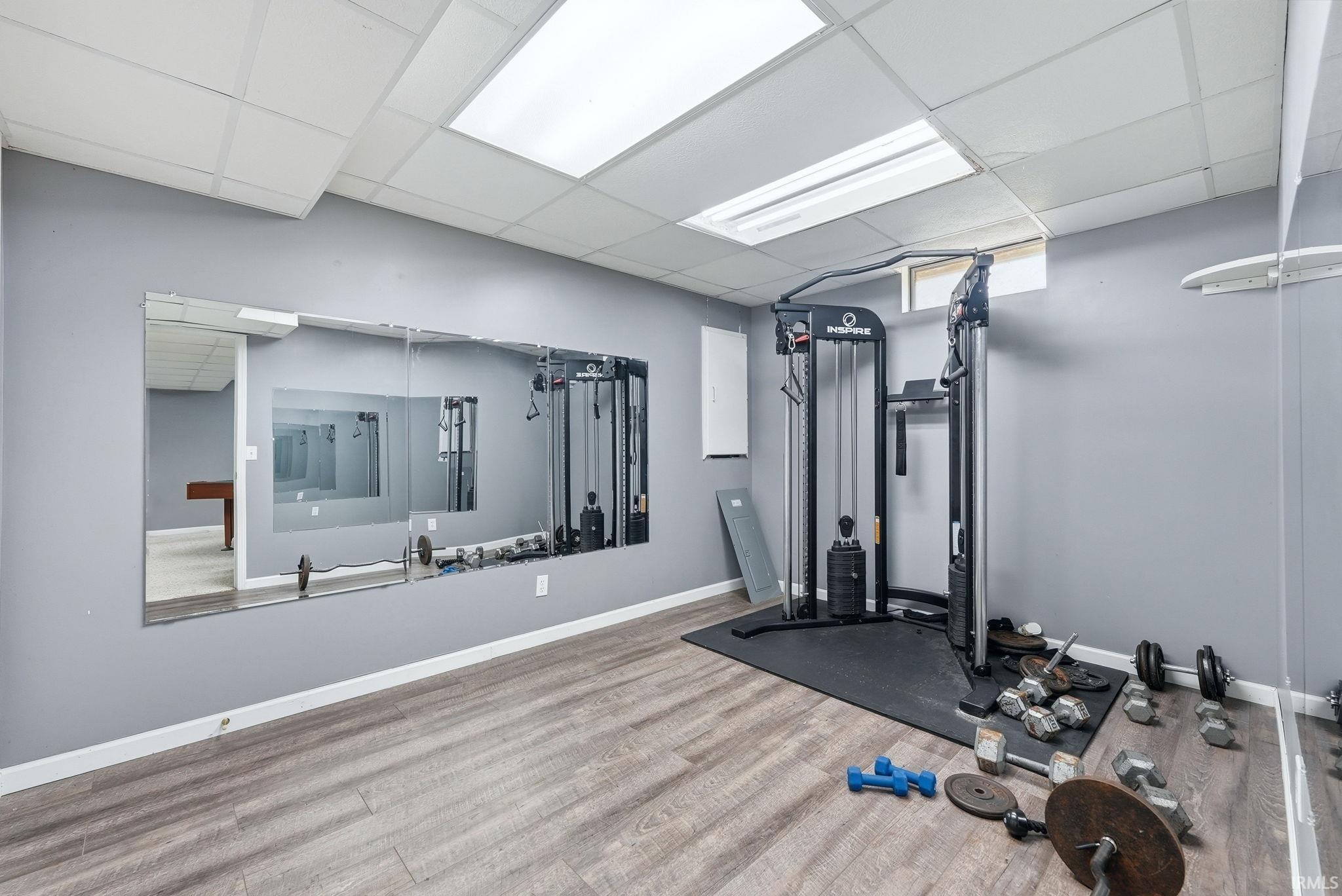 Dedicated fitness area featuring extensive mirrored walls, wood-finish flooring, recessed lighting, and a drop-tile ceiling
