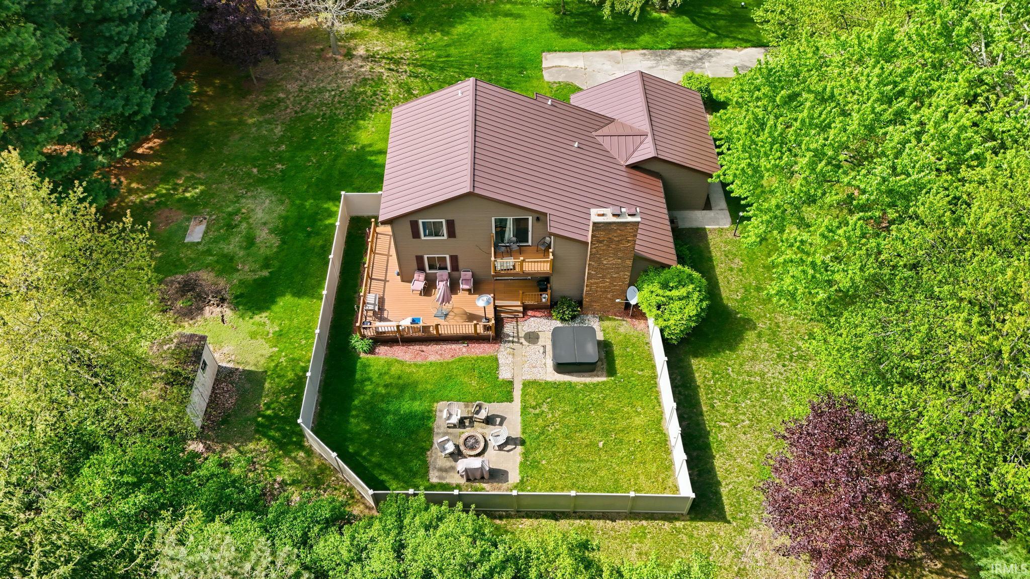 Aerial perspective showcasing a property with a brown-toned metal roof, a multi-level deck, and a fenced backyard