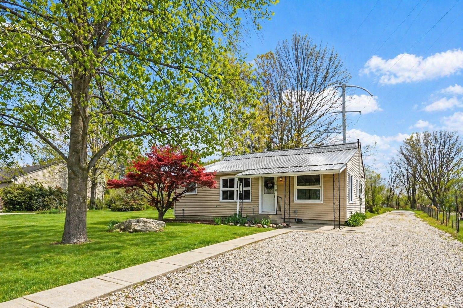 Single-story home featuring light-colored siding, a metal roof, and a gravel driveway