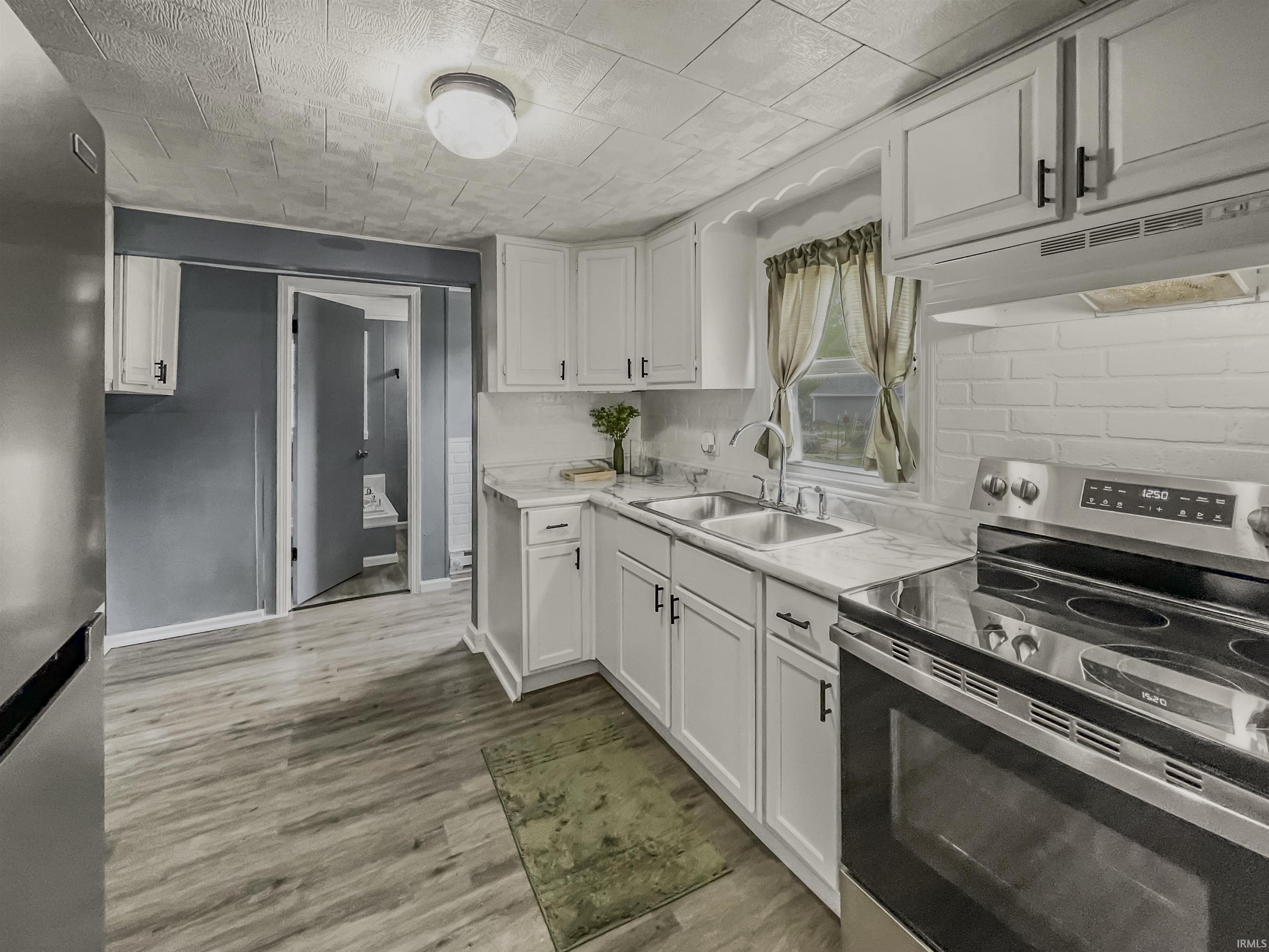 Kitchen featuring white cabinetry, wood-finish flooring, white subway tile backsplash, and stainless steel appliances