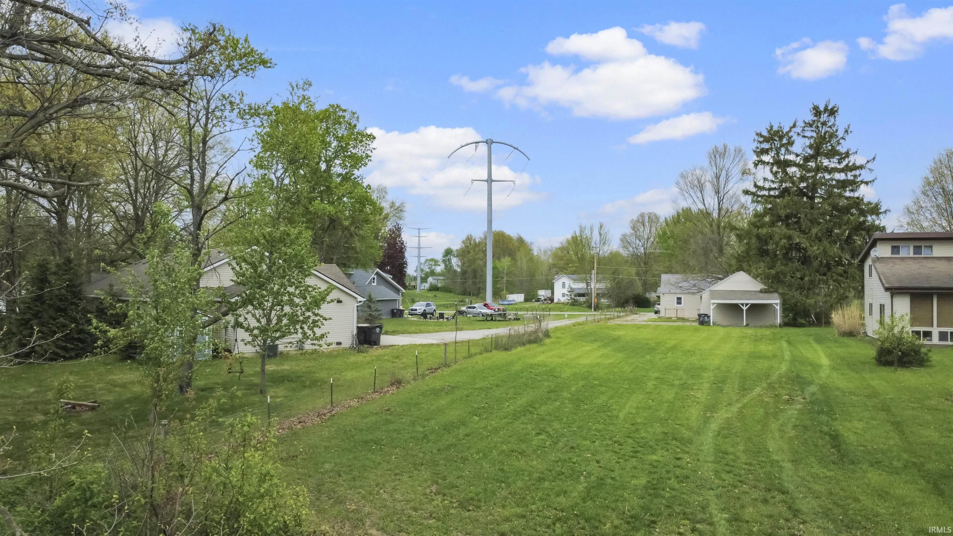 Expansive green space featuring a large lawn area, mature trees, and a visible carport structure