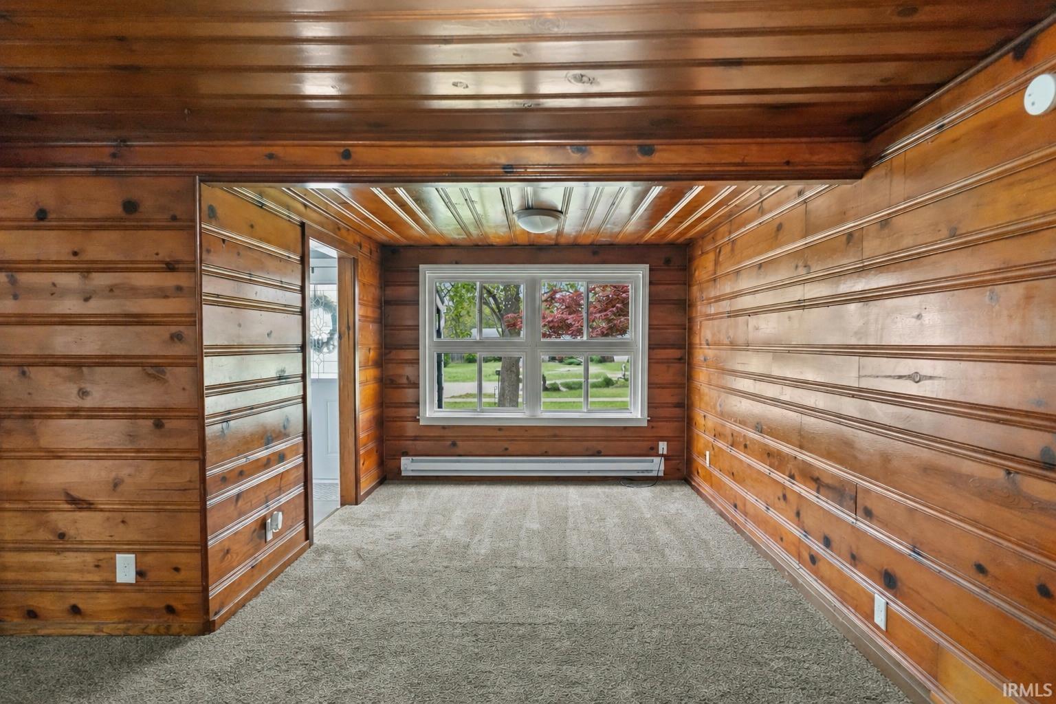 Room featuring extensive wood-paneled walls and ceiling, a large window, and light gray carpeting