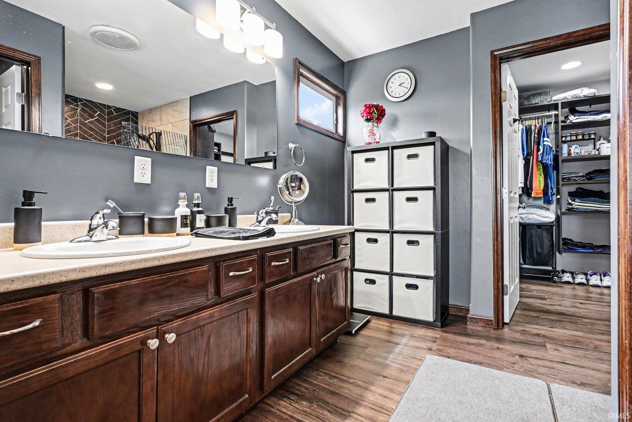 Bathroom featuring a double vanity with wood-finish cabinetry, light-toned countertops, and a long mirror