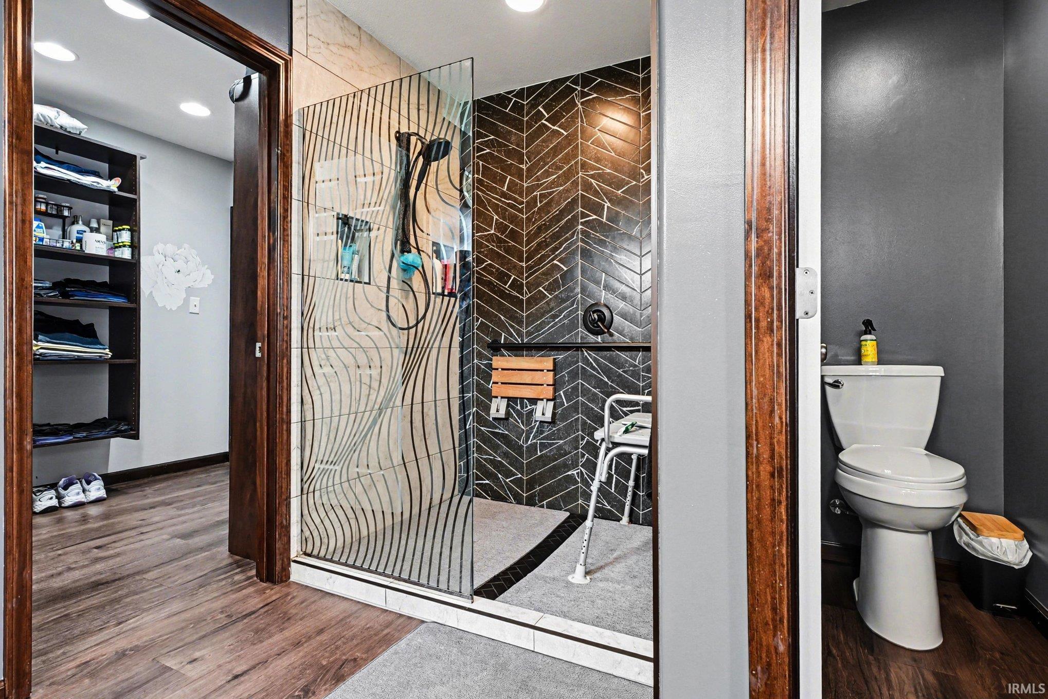 Spa-inspired shower with black herringbone tile, a built-in wooden bench, and a unique textured glass enclosure
