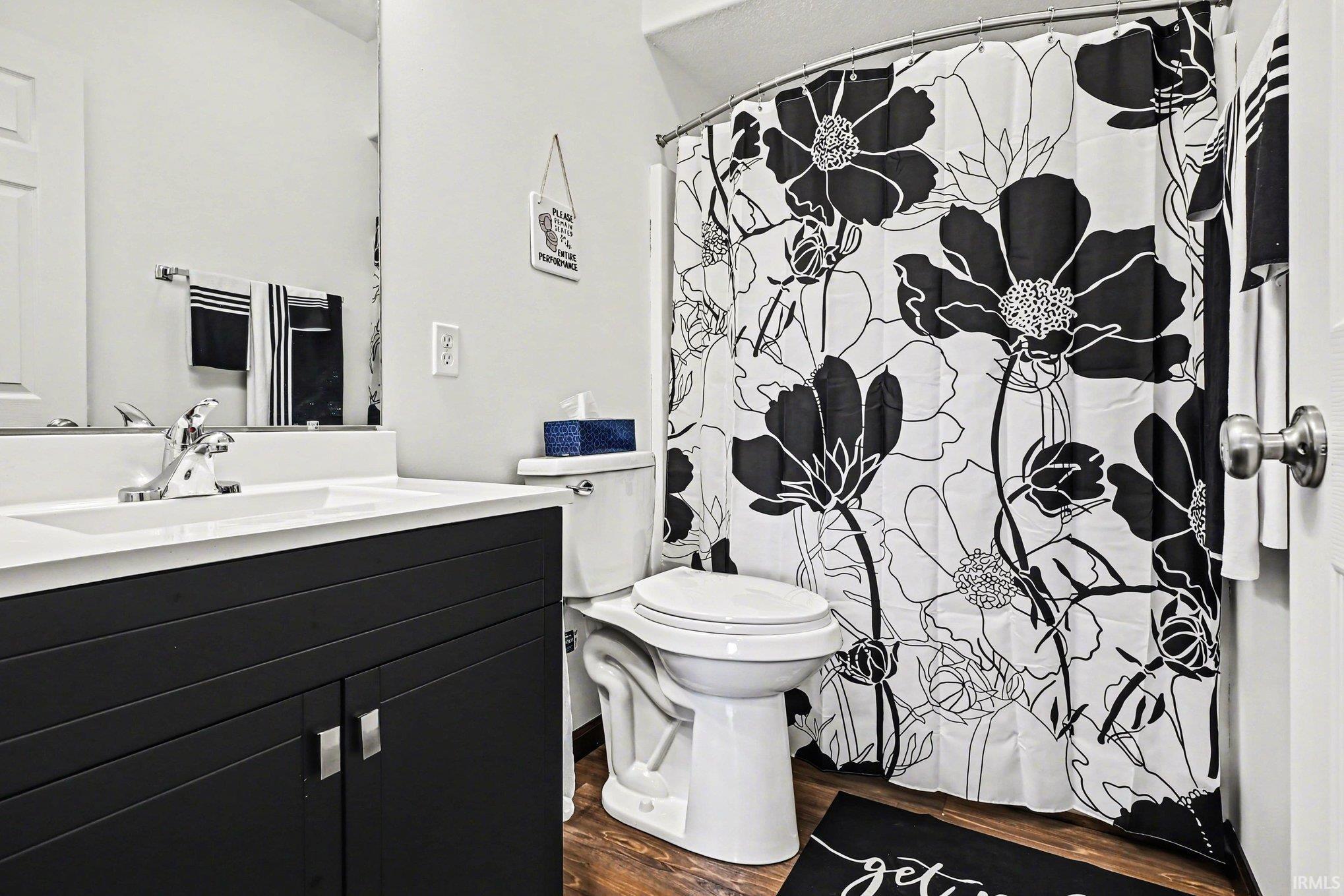Bathroom featuring a dark wood-finish vanity with chrome hardware, an integrated white sink, a chrome faucet, and wood-finish flooring