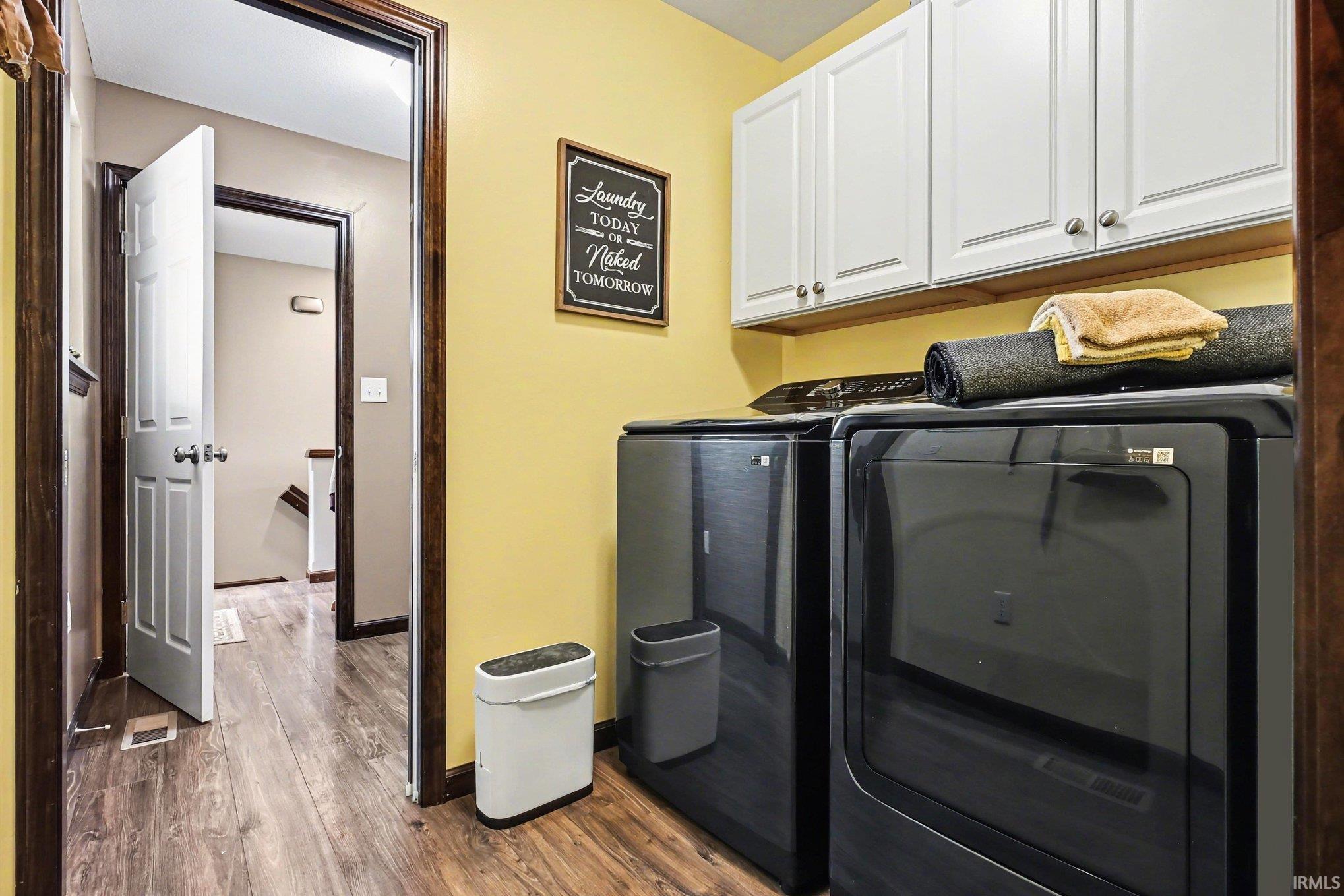 Dedicated laundry area featuring wood-finish flooring, white overhead cabinetry with brushed nickel hardware, and vibrant yellow walls