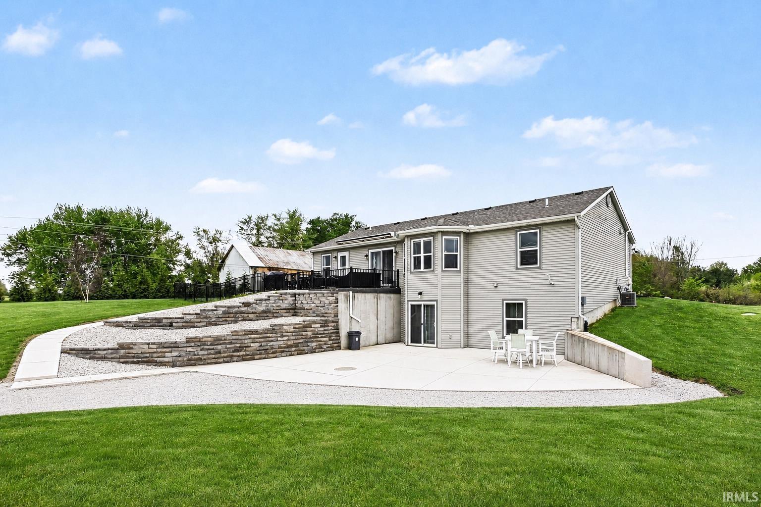 Expansive rear exterior featuring a concrete patio, tiered retaining walls, and a manicured lawn